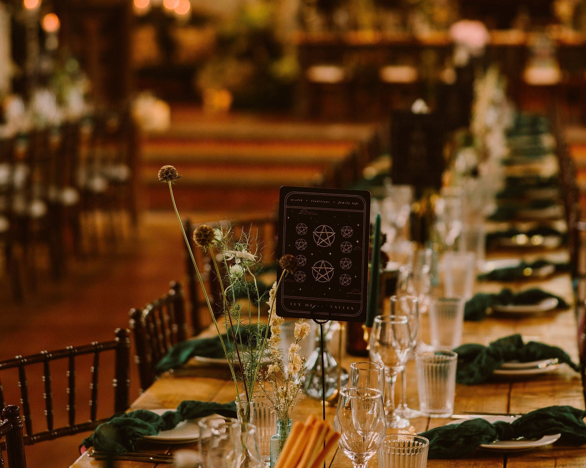 Tarot card seating chart in soft pastels behind a banquet table with green napkins and glasses