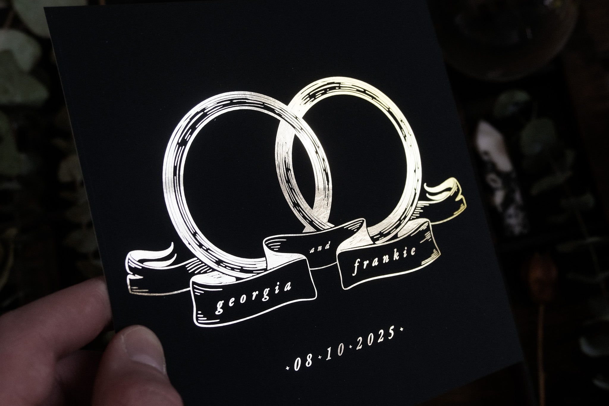 A hand displays a luxury UK wedding save the date card with interlocking foiled rings on premium cardstock, exuding romantic elegance.