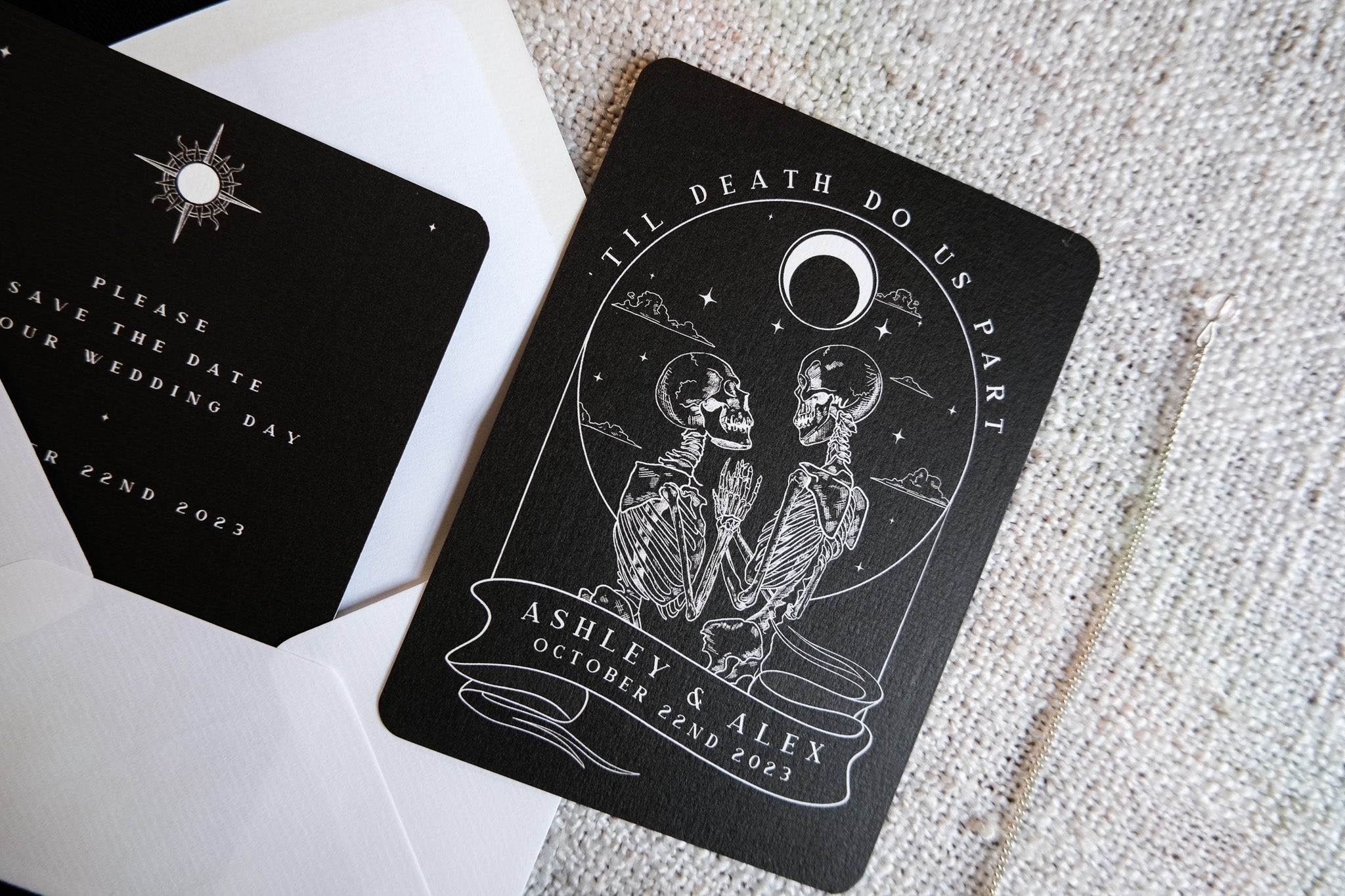 Luxury UK wedding stationery save the date featuring gothic skeleton lovers and crescent moon on dramatic black card with celestial motif.