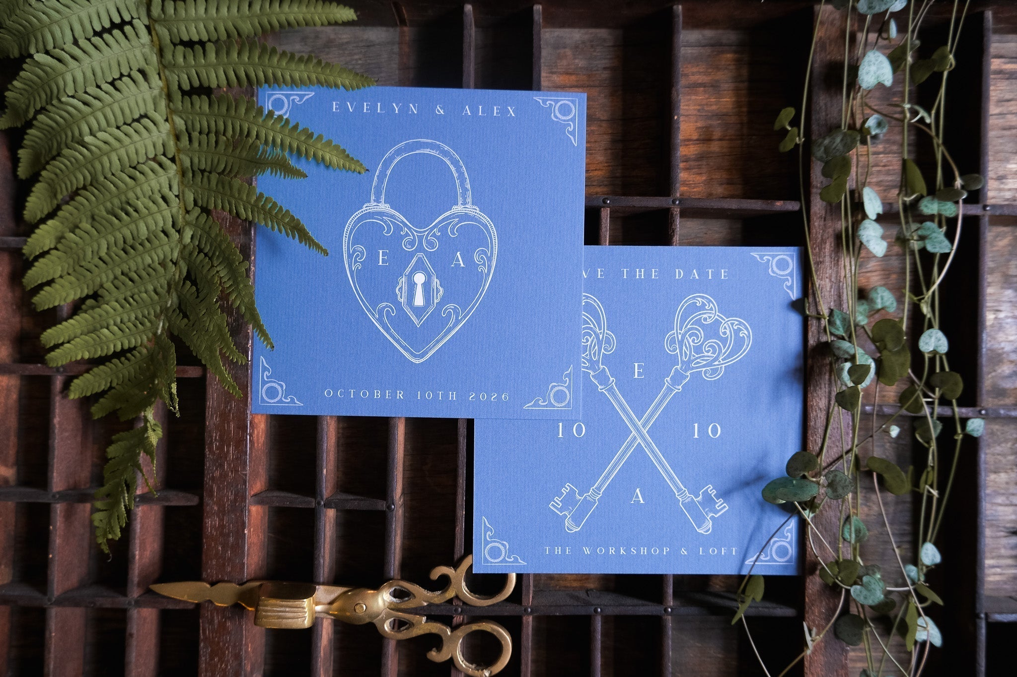 Luxury vintage wedding stationery in deep blue with gothic skeleton keys, styled with ferns and brass scissors on rustic wood.