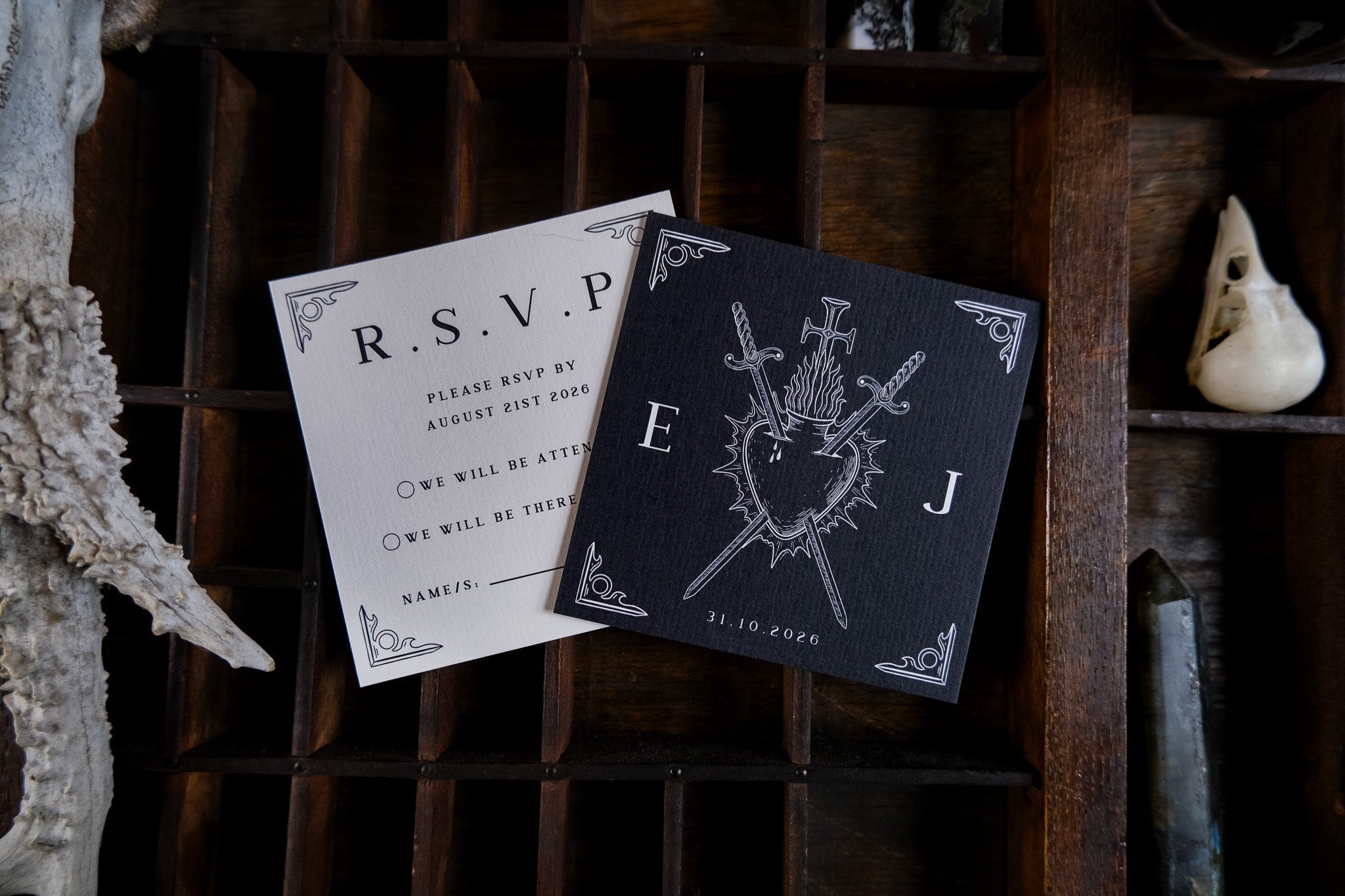 Luxury gothic wedding stationery suite featuring a black crested invitation and white RSVP card on a wooden tray, dramatic and romantic.