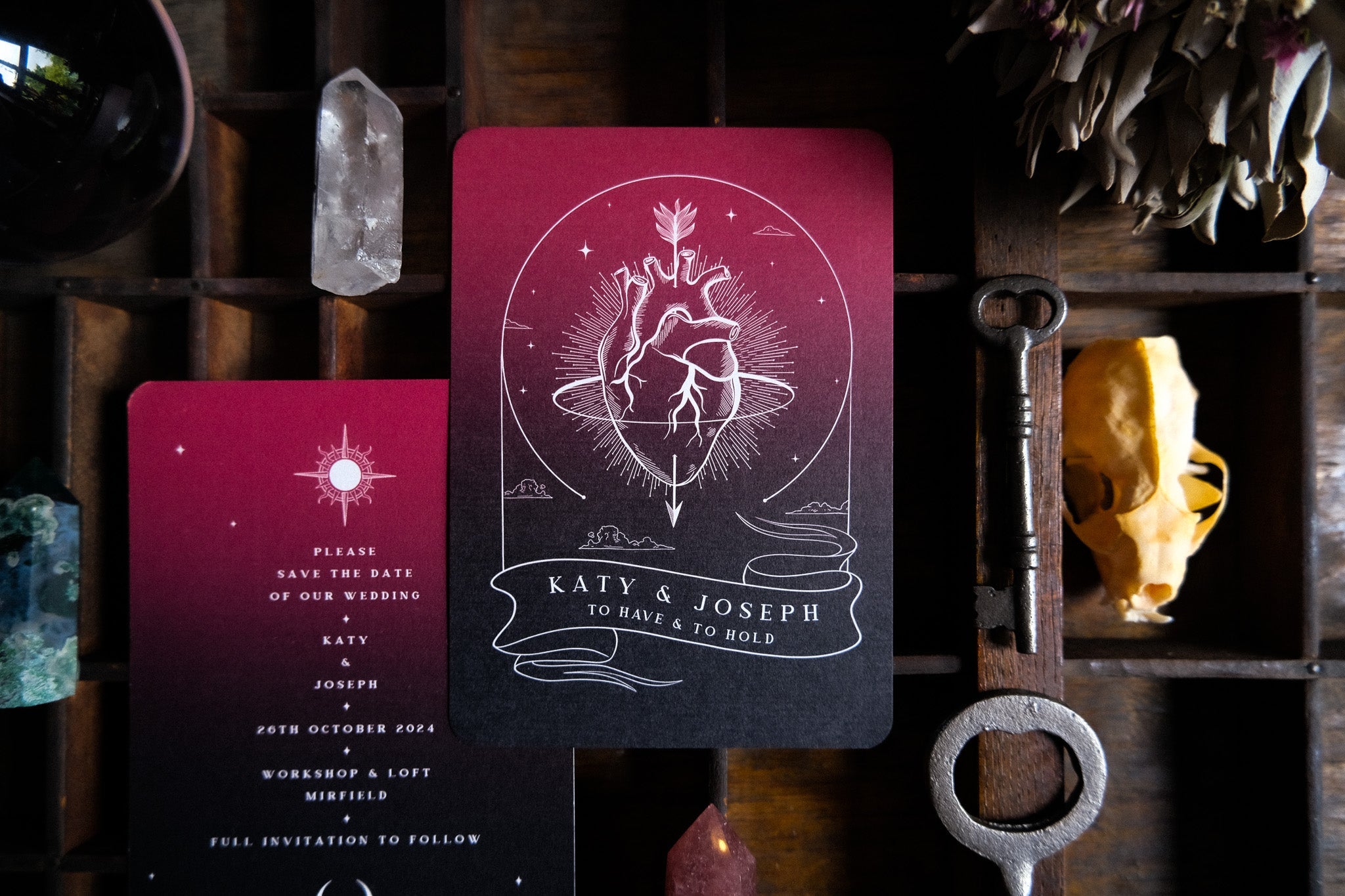 A6 gothic Save the Date cards with anatomical heart motif on a wooden tray, accented by crystals and vintage key—luxury UK alternative wedding stationery.