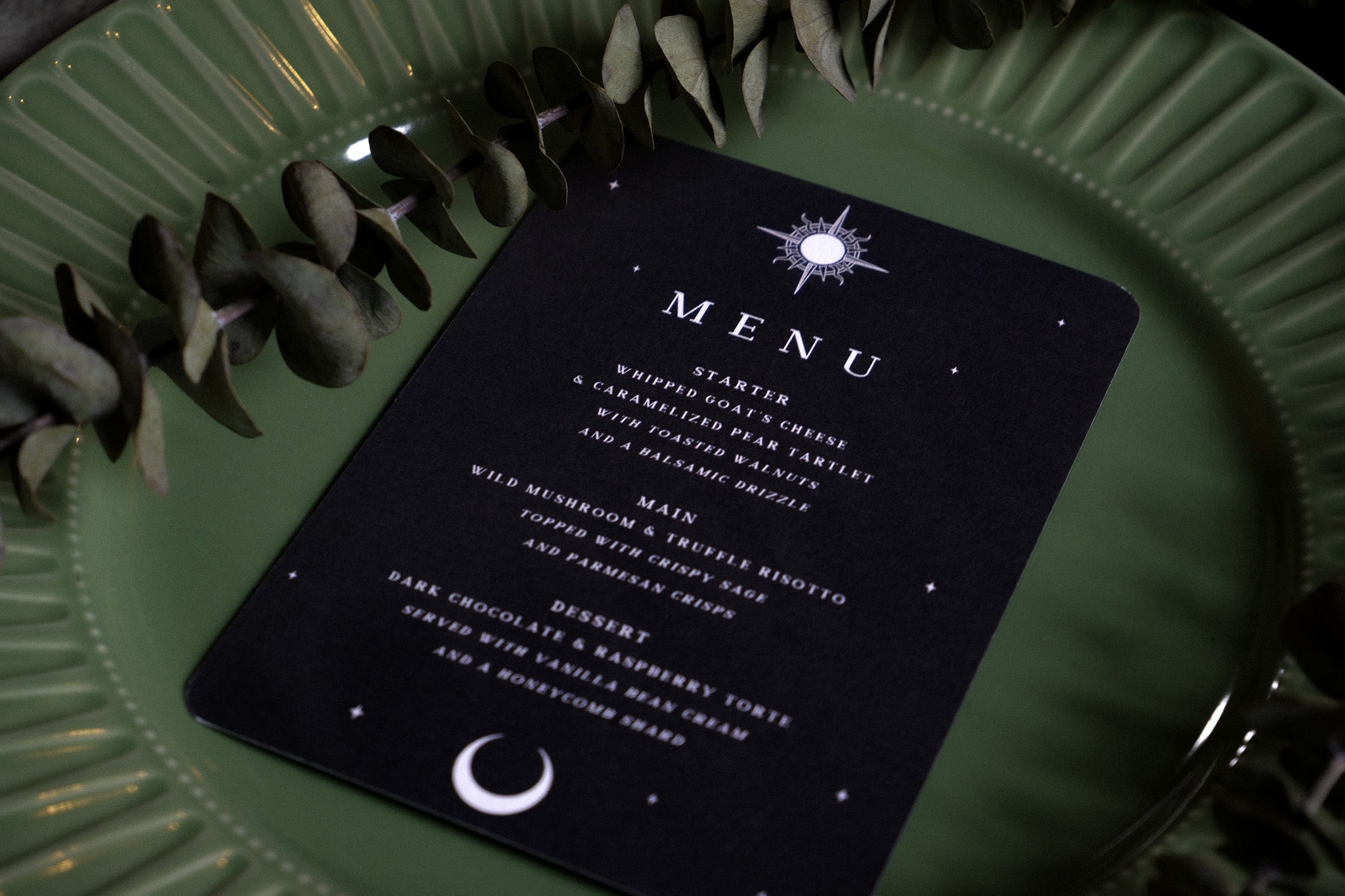 Luxury gothic wedding menu card with skeleton couple and celestial motifs, set on green plate with greenery for a dramatic UK vibe.