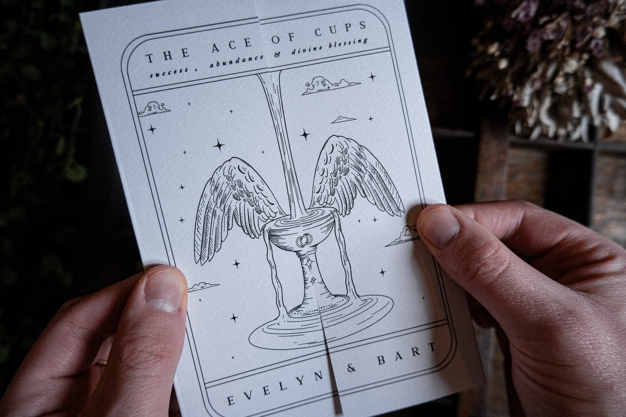 A person holds a luxury celestial gatefold wedding invitation with tarot and mystical motifs, featuring foil details and winged cup design.