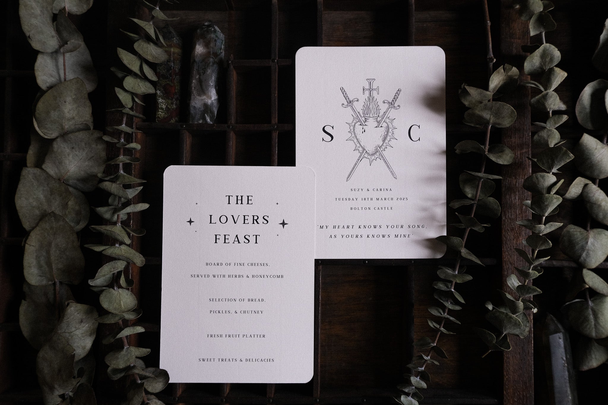 Luxury vintage-inspired wedding menus with dramatic gothic artwork, displayed on dark wood with dried leaves for an alternative UK style.