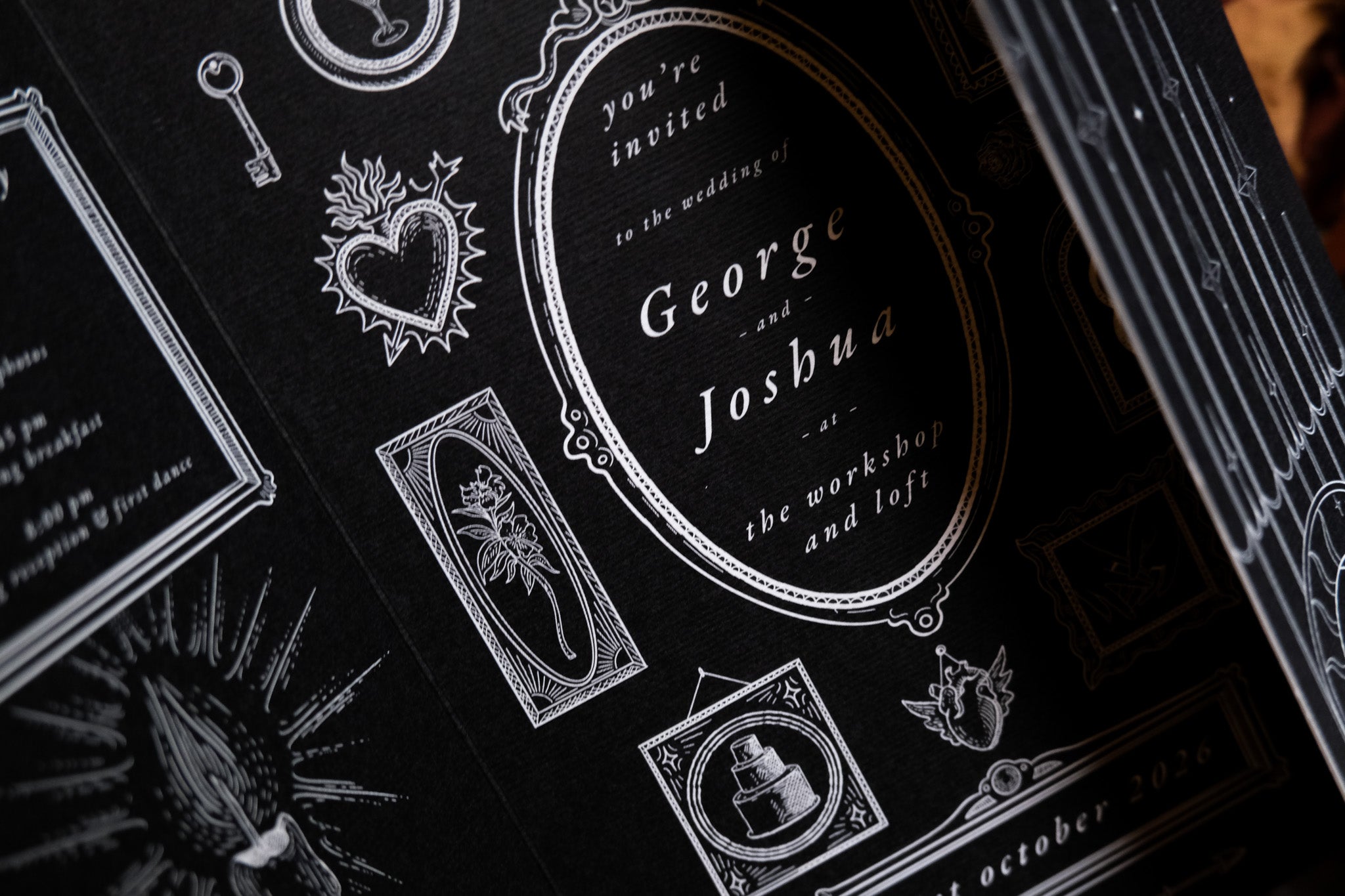 Close-up of a luxury gatefold wedding invitation with ornate white gothic motifs on dark cardstock, perfect for dramatic UK weddings.