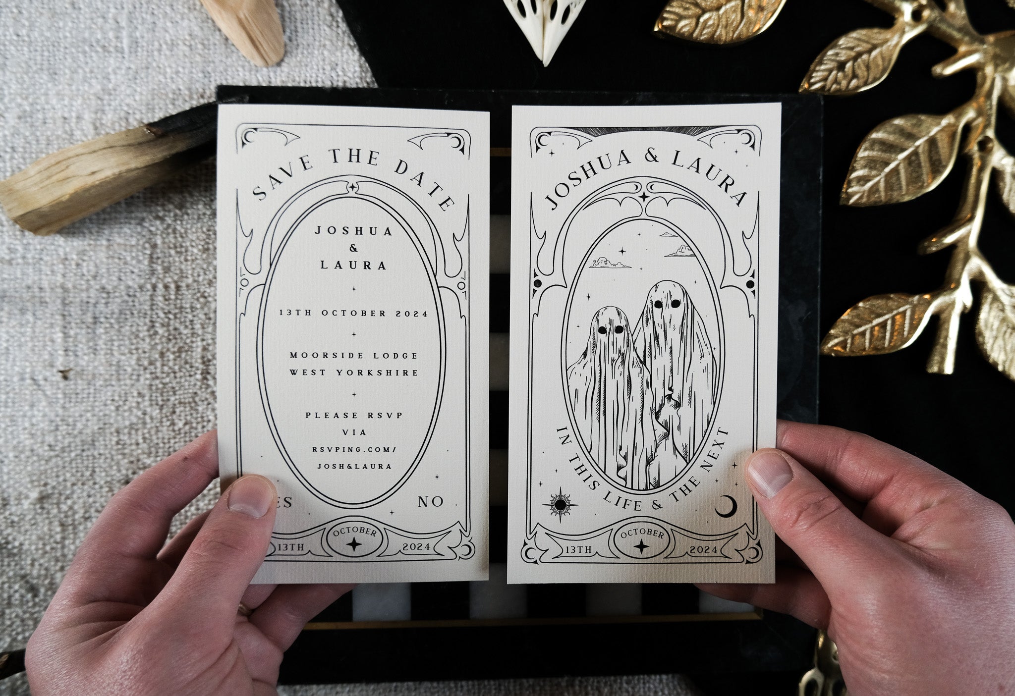Two hands display luxury UK gothic wedding save the date cards with ghostly figures beneath an ornate arch; dramatic, alternative style.