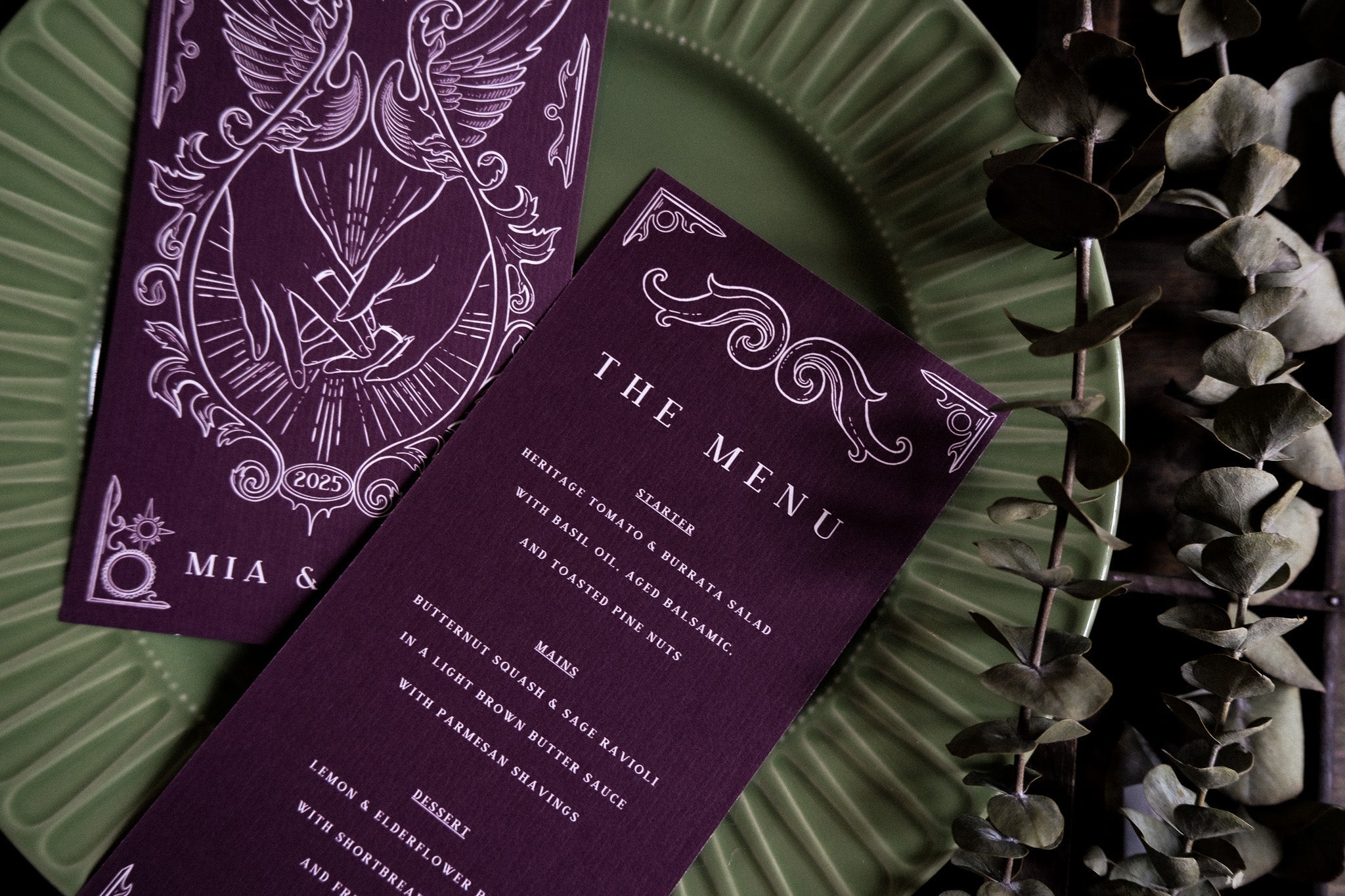 Luxury gothic tarot-inspired wedding menu cards in deep purple with white details, on a green plate with dried eucalyptus, UK stationery.