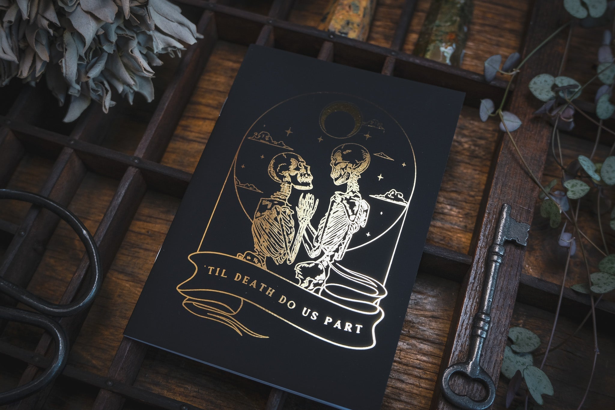 Luxury UK wedding stationery card in dramatic gothic style, with gold foil celestial skeletons and mystical vintage detailing on black.