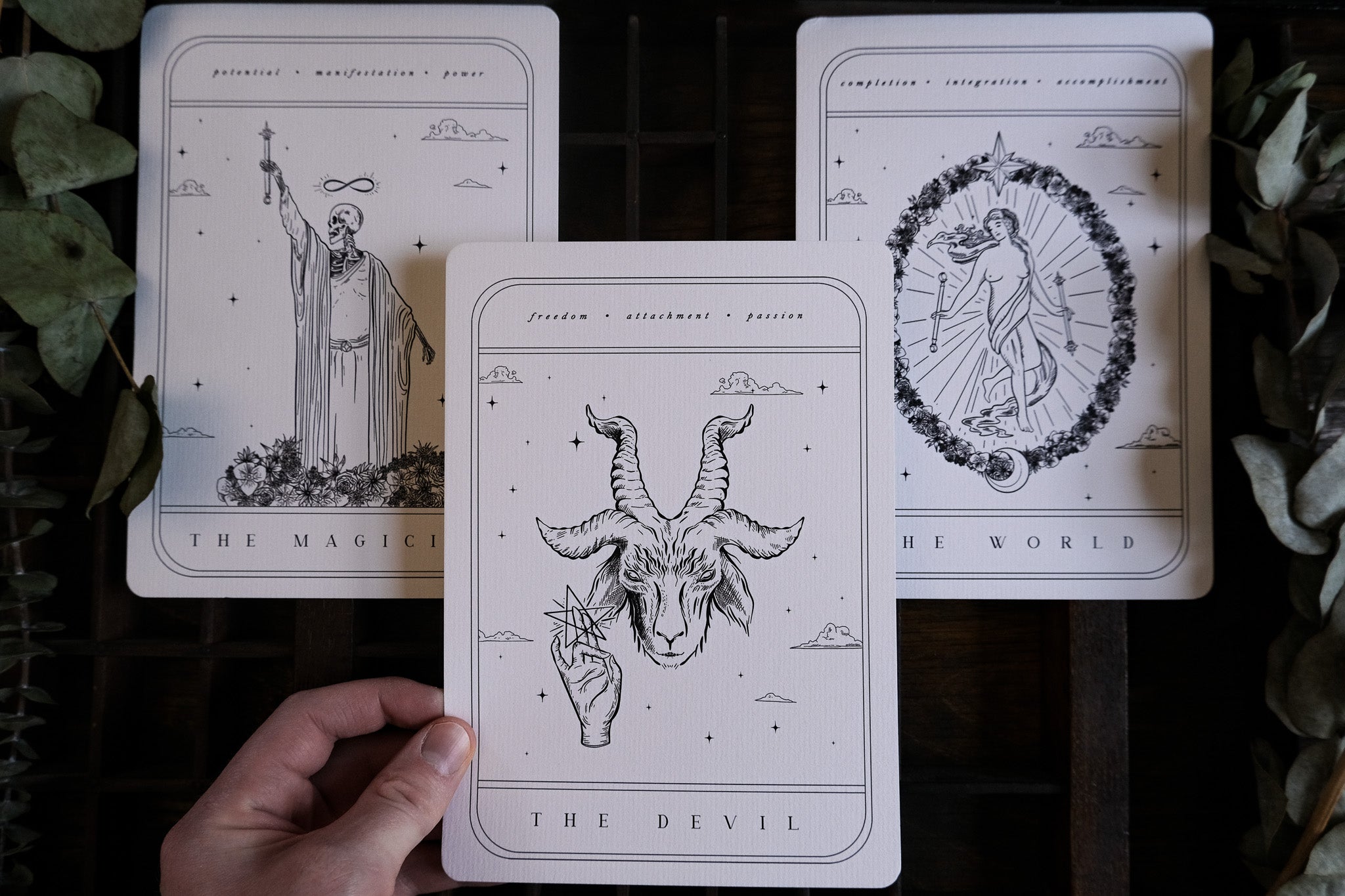 A hand displays luxurious gothic wedding stationery with a dramatic tarot card design, detailed vintage art, and mystical accents.
