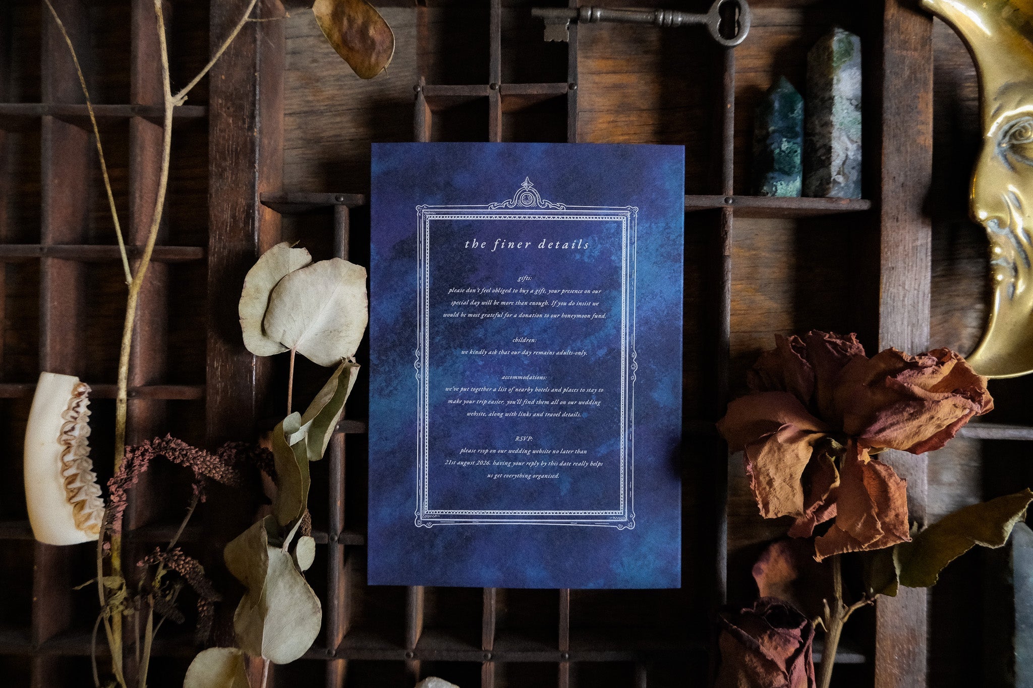 Luxury gatefold wedding invitation with gothic silhouette design, styled on wood with dried flowers, crystals, key and gold mask.