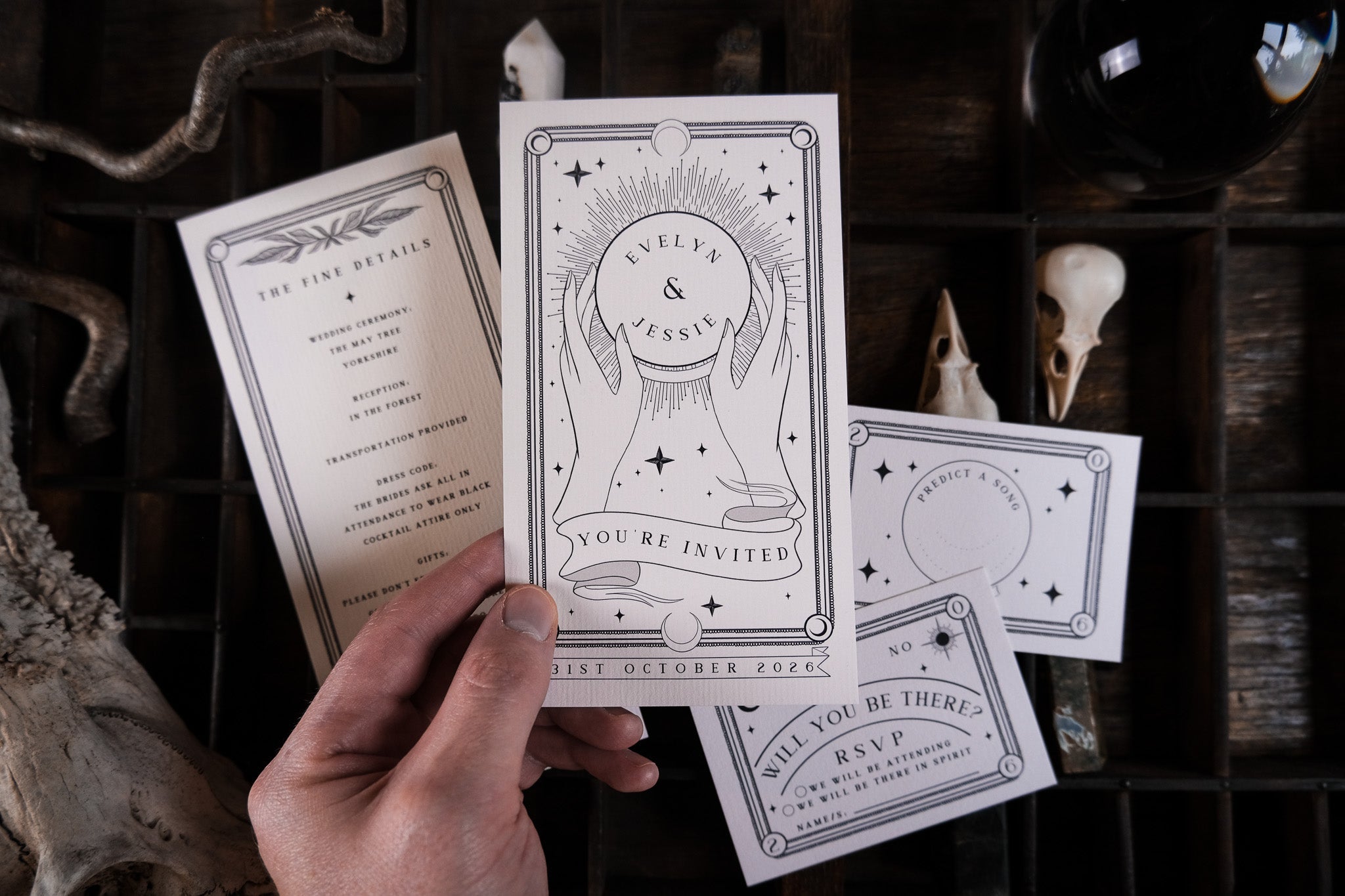 A hand displays a gothic, celestial wedding stationery set in luxe black and white with star motifs, styled on dark wood for a dramatic UK vibe.