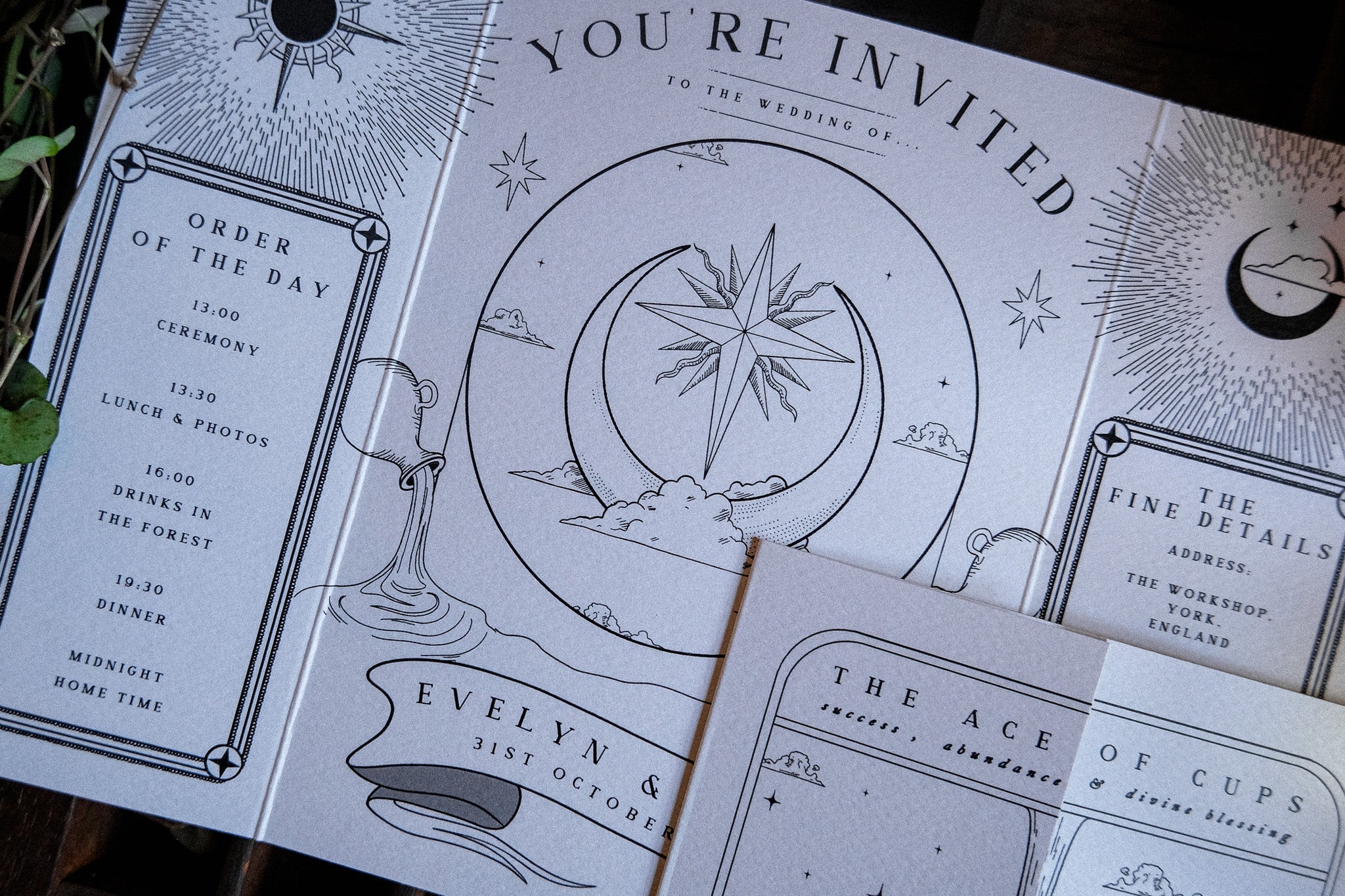 Close-up of a luxury gatefold wedding invitation with mystical tarot-inspired celestial motifs in dramatic black ink on crisp white card.