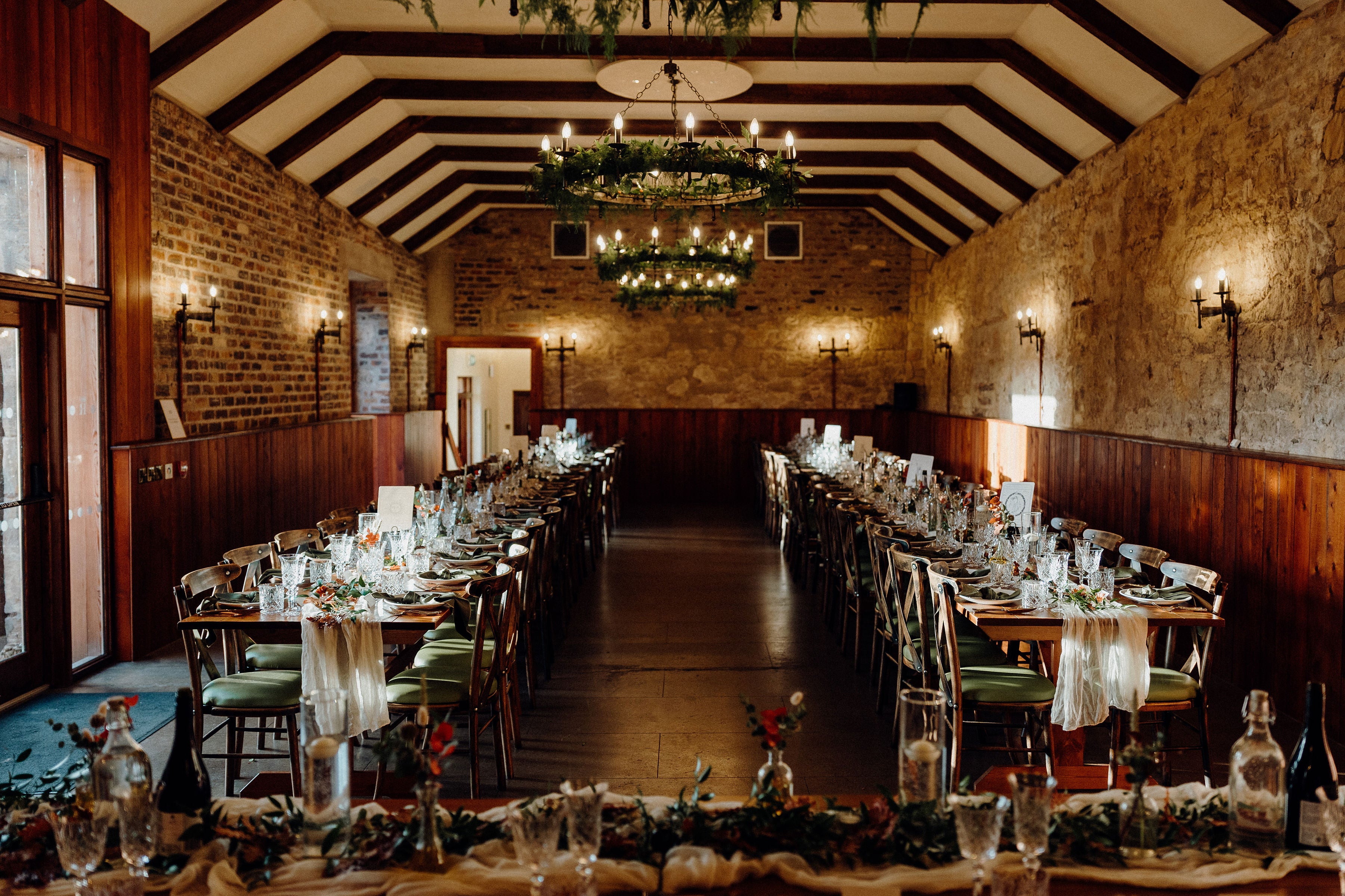 Luxury personalised wedding stationery with a romantic, vintage design graces rustic tables in a warm, candlelit UK banquet hall.
