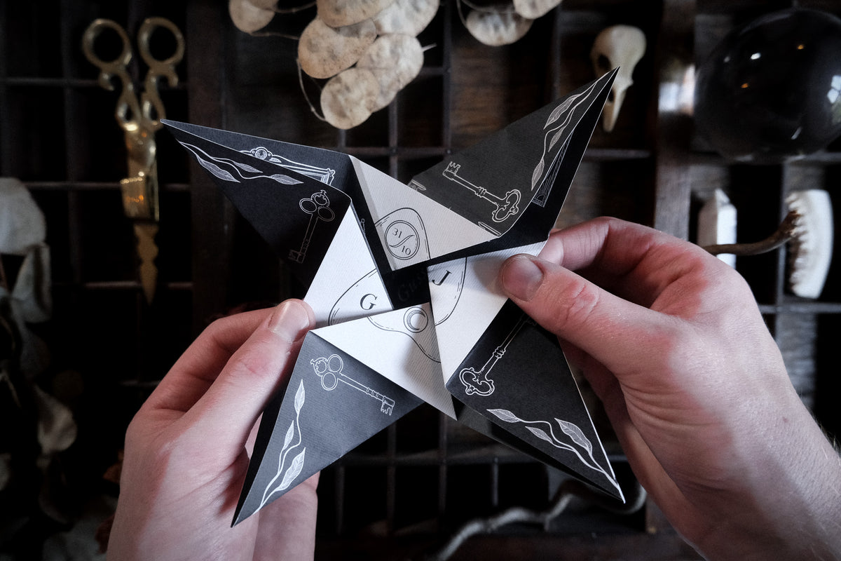 A black and white self-fold Victorian wedding invitation featuring hand illustrations, shown on dark wood with dried plants.