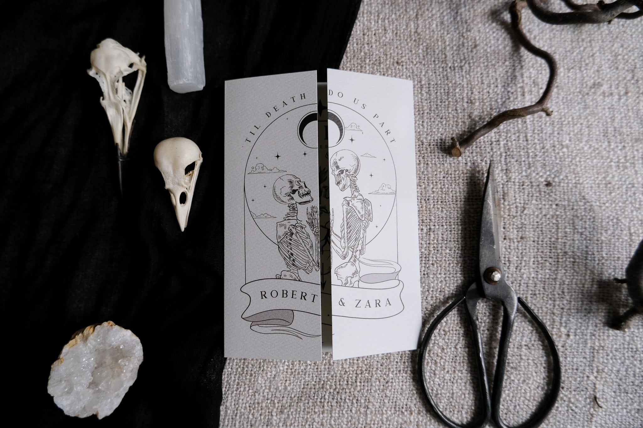 Skeleton Lovers & Bleeding Heart Til Death Do Us Part wedding invitation with gothic design, displayed on a textured surface with artistic elements.