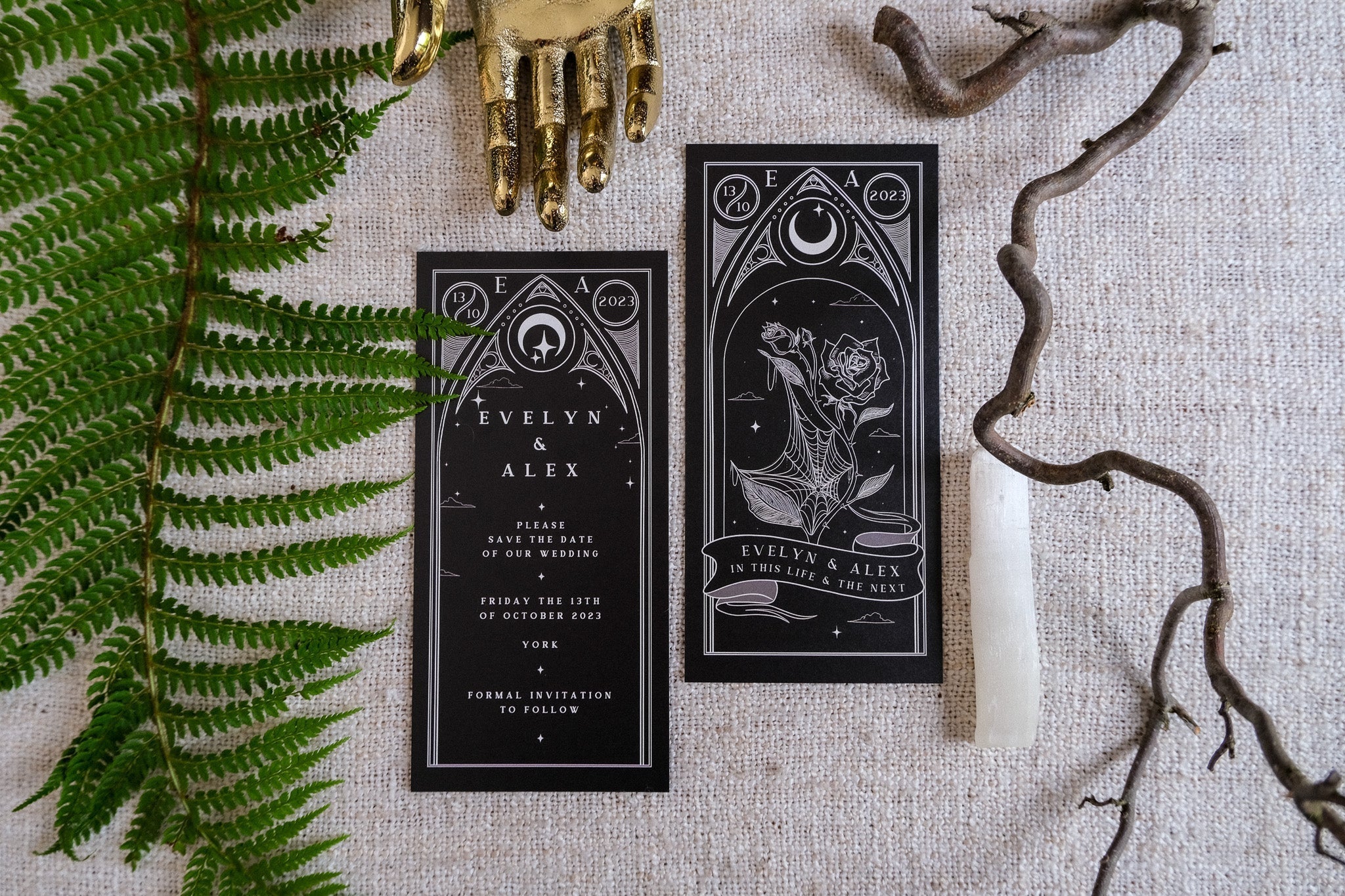 Black Rose Tarot Save The Date Card with elegant design featuring moon and rose motifs, paired with a white envelope on a textured surface, surrounded by natural elements.