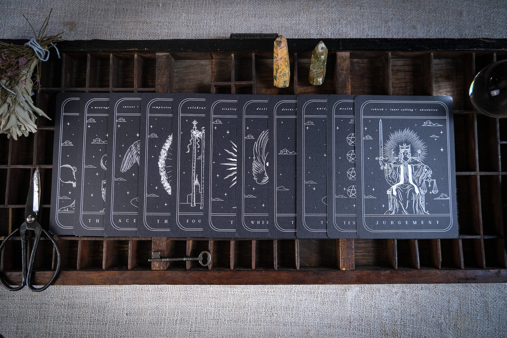 Set of gothic tarot card art prints with black background and white mystical illustrations displayed in a wooden tray for wedding decor and seating charts