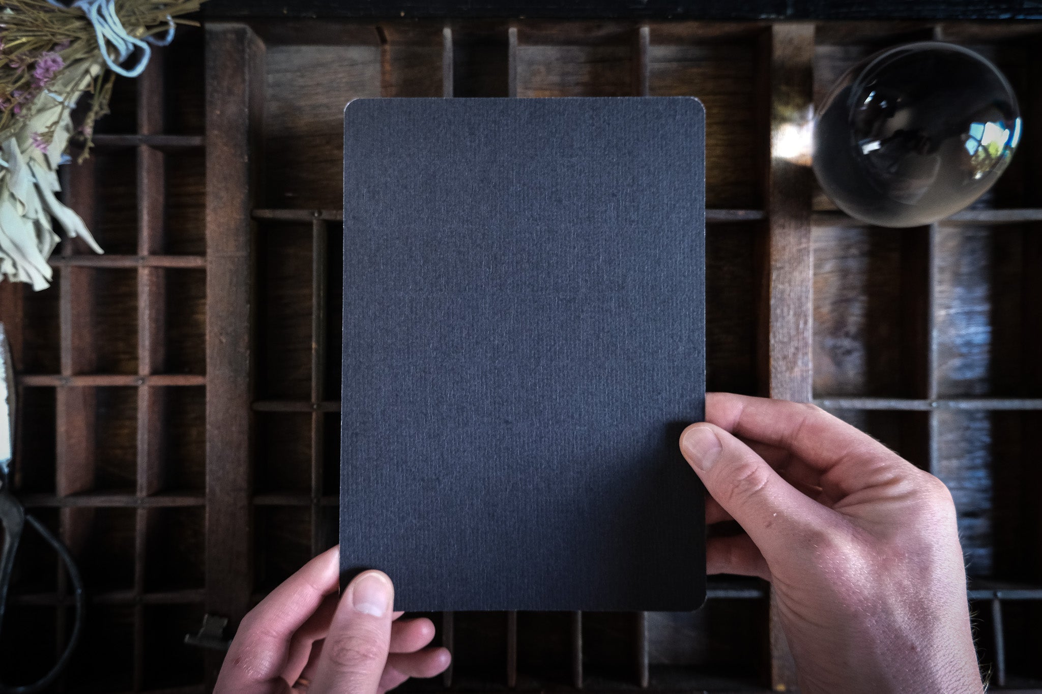 Hand holding blank black matte tarot card art print with rounded edges over wooden surface