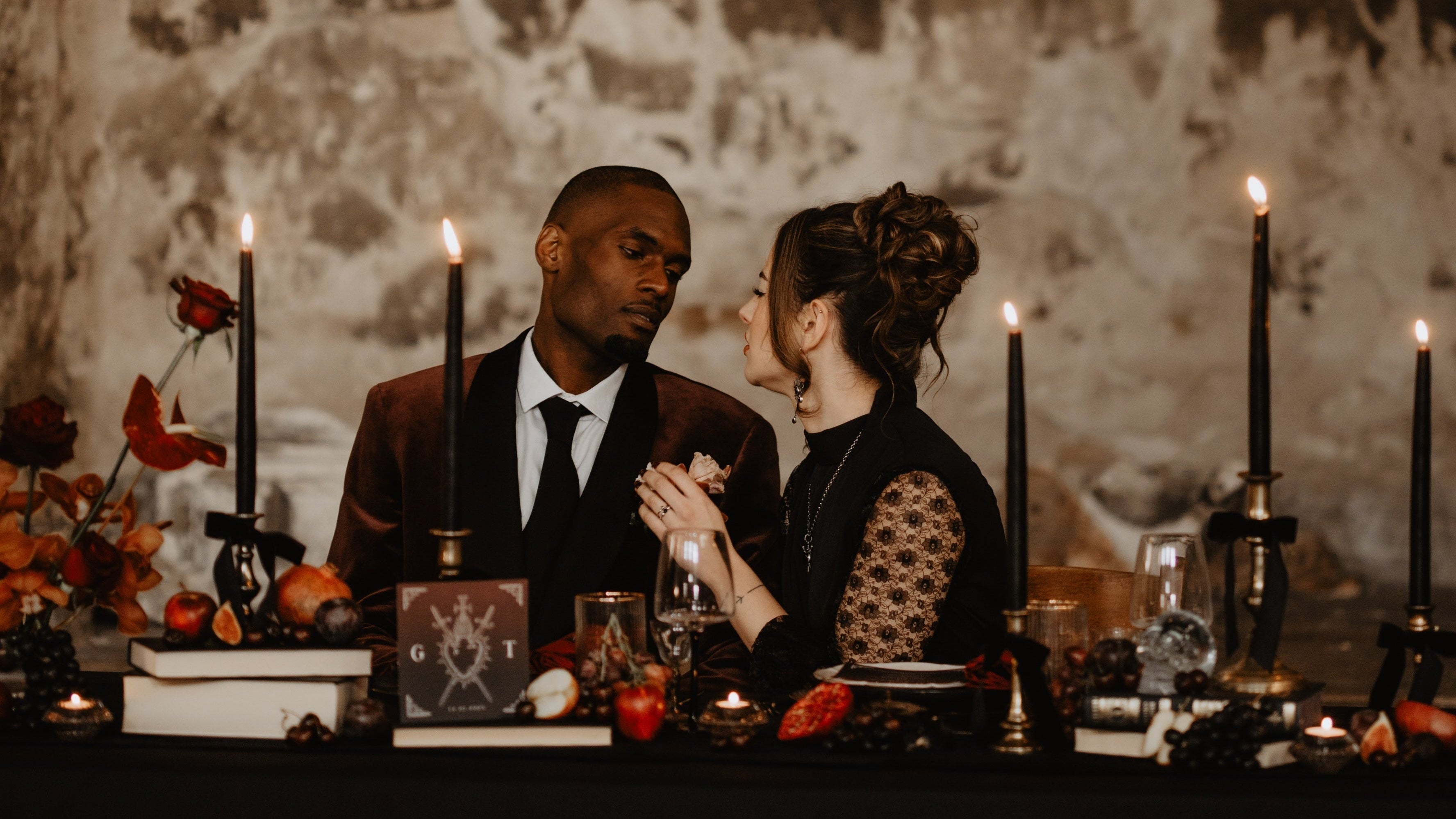 Halloween Wedding - Two people sitting at a table with candles and flowers in an old, rustic setting for a vintage wedding top table