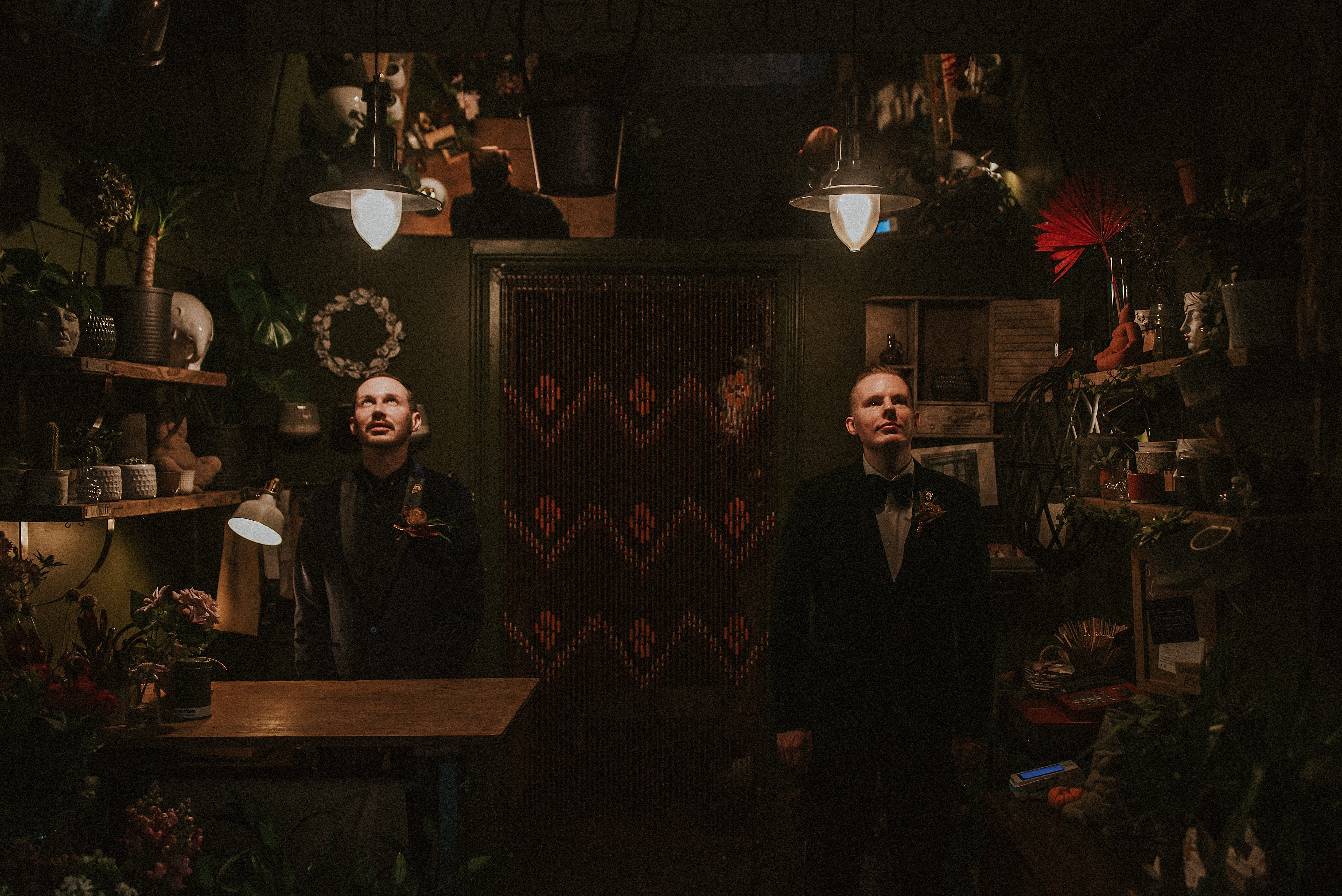 Two men in formal attire standing in a dimly lit room with decorative elements.