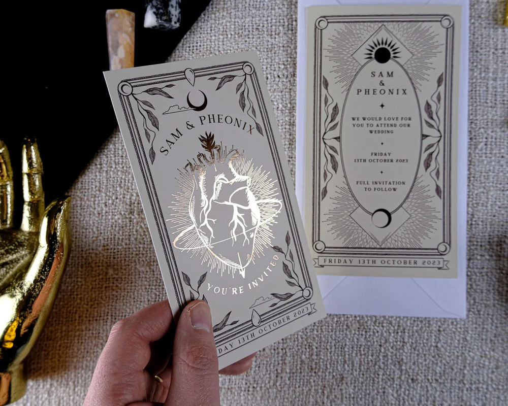 A hand displays luxury wedding stationery with gold foil accents, boho design, and romantic detailing, set beside a decorative gold hand.
