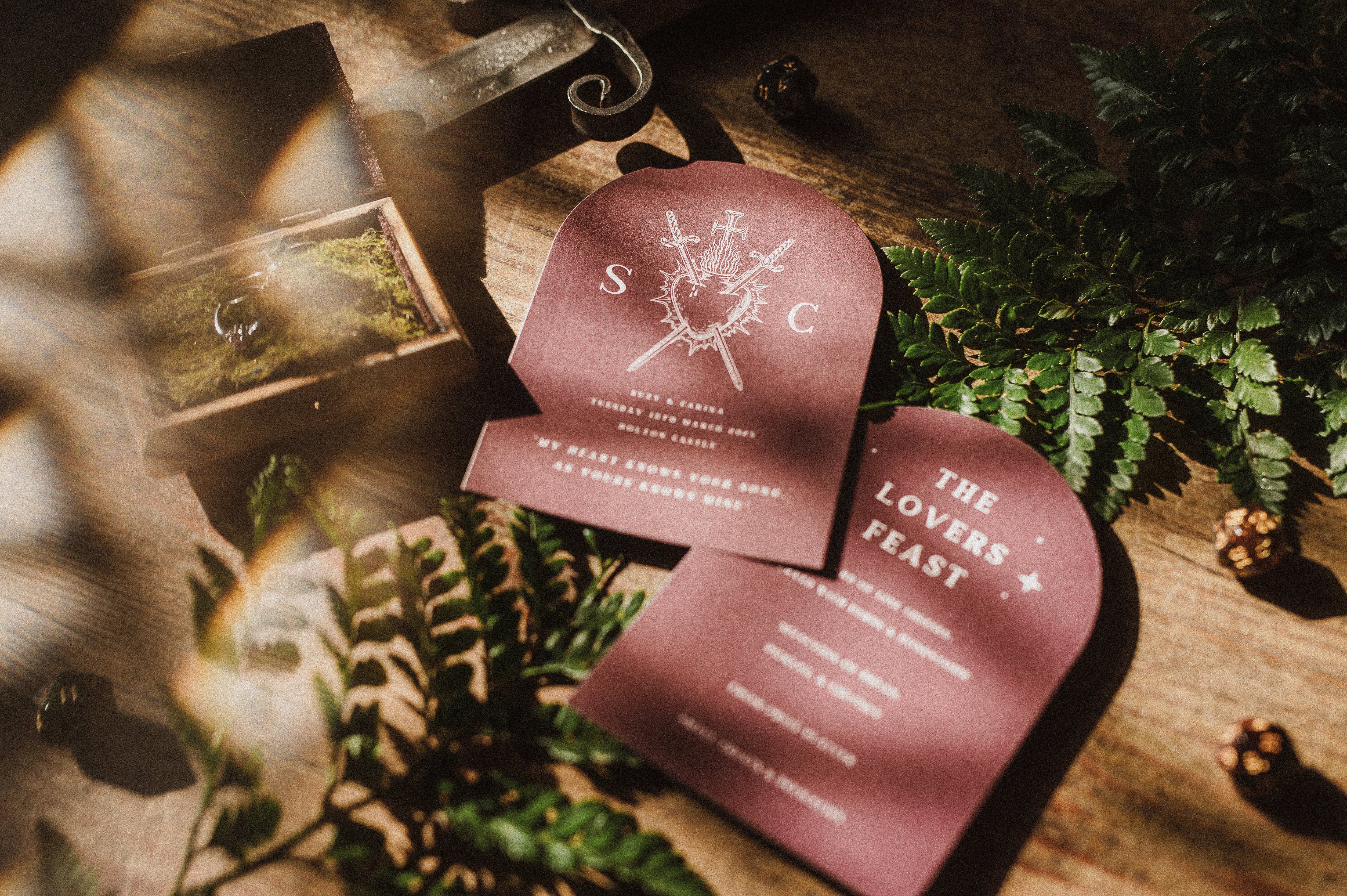 Dramatic arched wedding menus with white text and a bleeding heart motif, displayed on wood among vintage boho forest details.