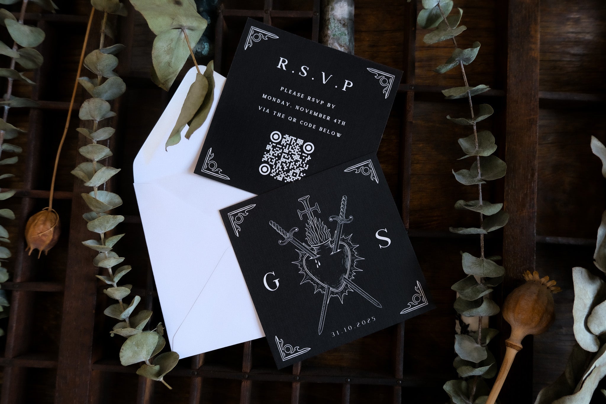 Luxury black square wedding RSVP cards in a dramatic gothic style on white envelope, styled with dried leaves and rustic wood.