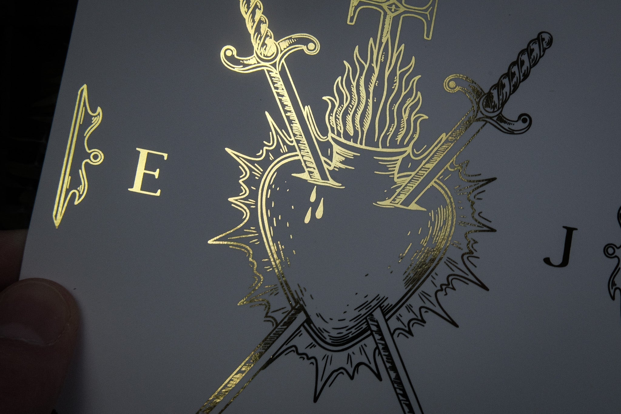Luxury UK save the date card with gold-foil bleeding heart, flaming swords, and hand motif on white—dramatic gothic wedding stationery.