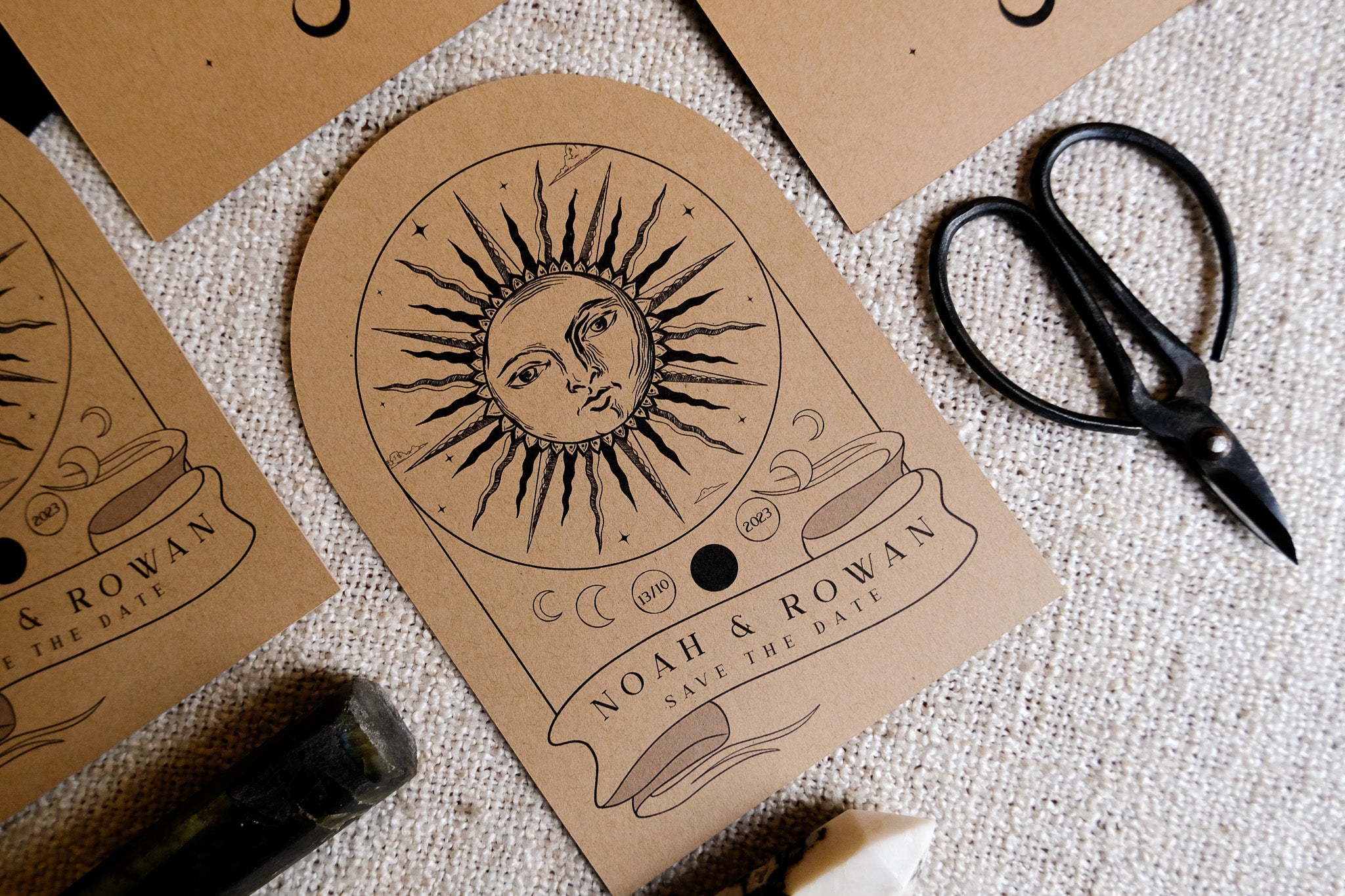 Luxury celestial wedding stationery with hand-drawn sun and moons on kraft arched card, styled with vintage scissors and crystal.