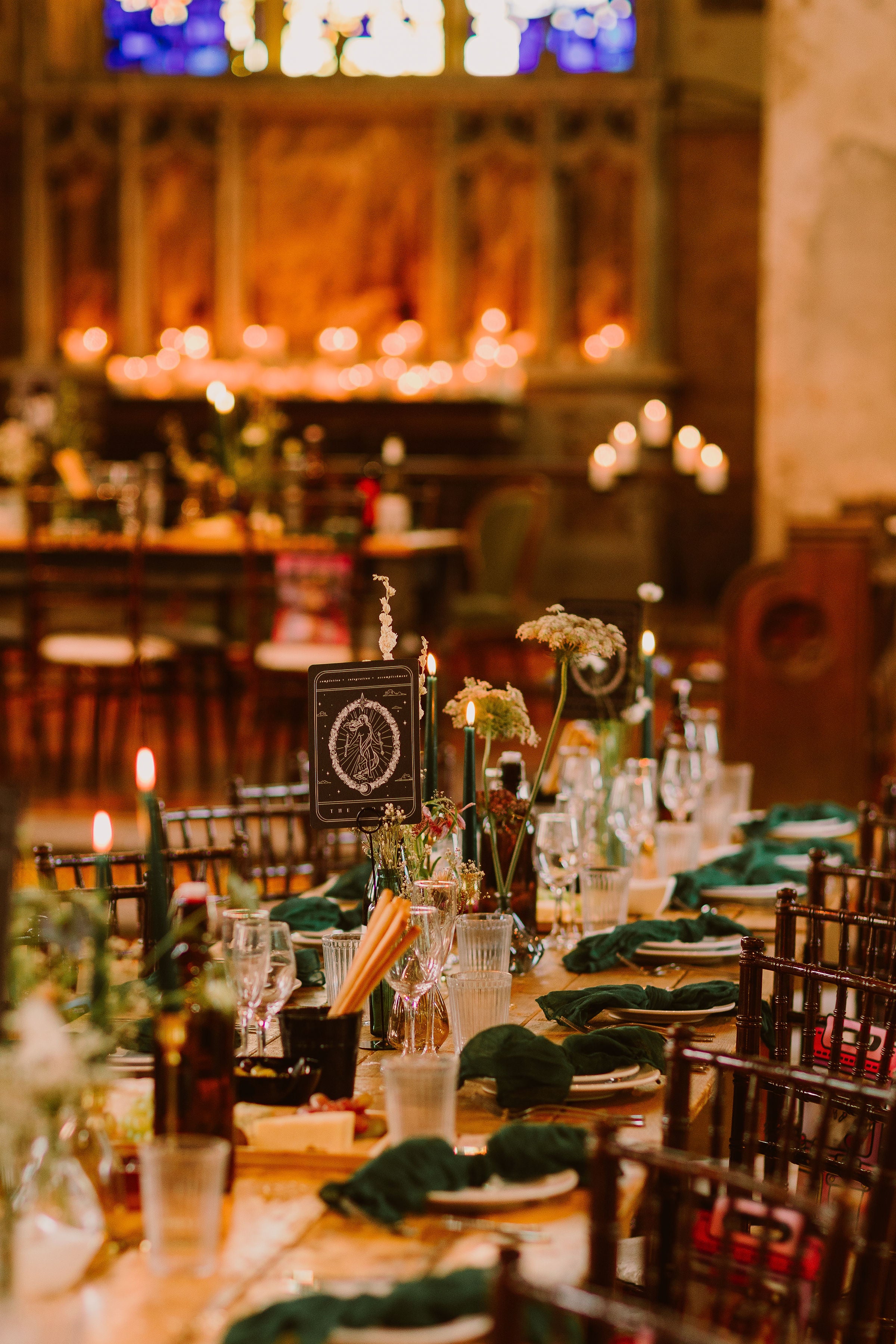 Luxury UK wedding stationery with green accents on an elegantly set table, candles, vintage glassware, and a romantic gothic setting.
