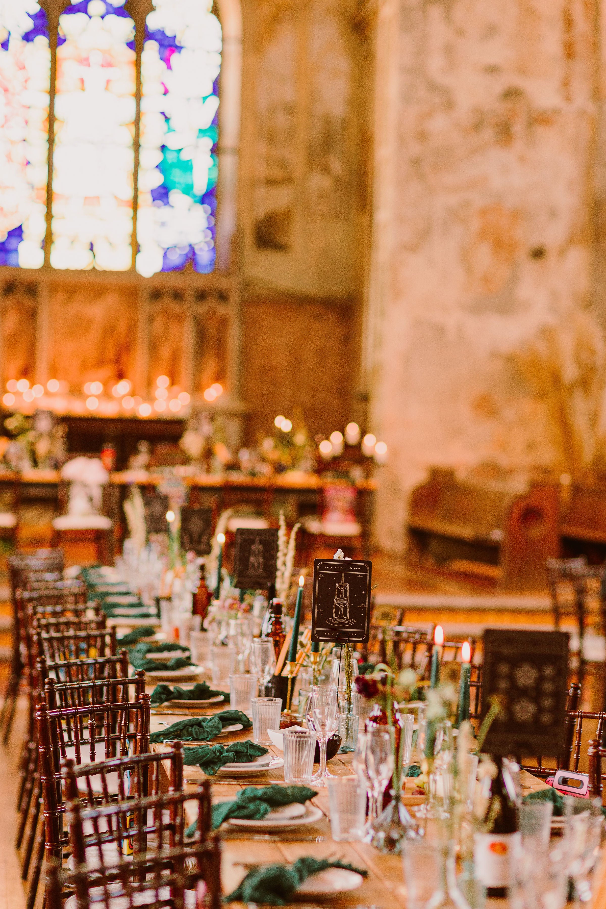Luxury UK wedding stationery with dramatic table numbers on premium card, set amid candles in a rustic venue with stained glass windows.