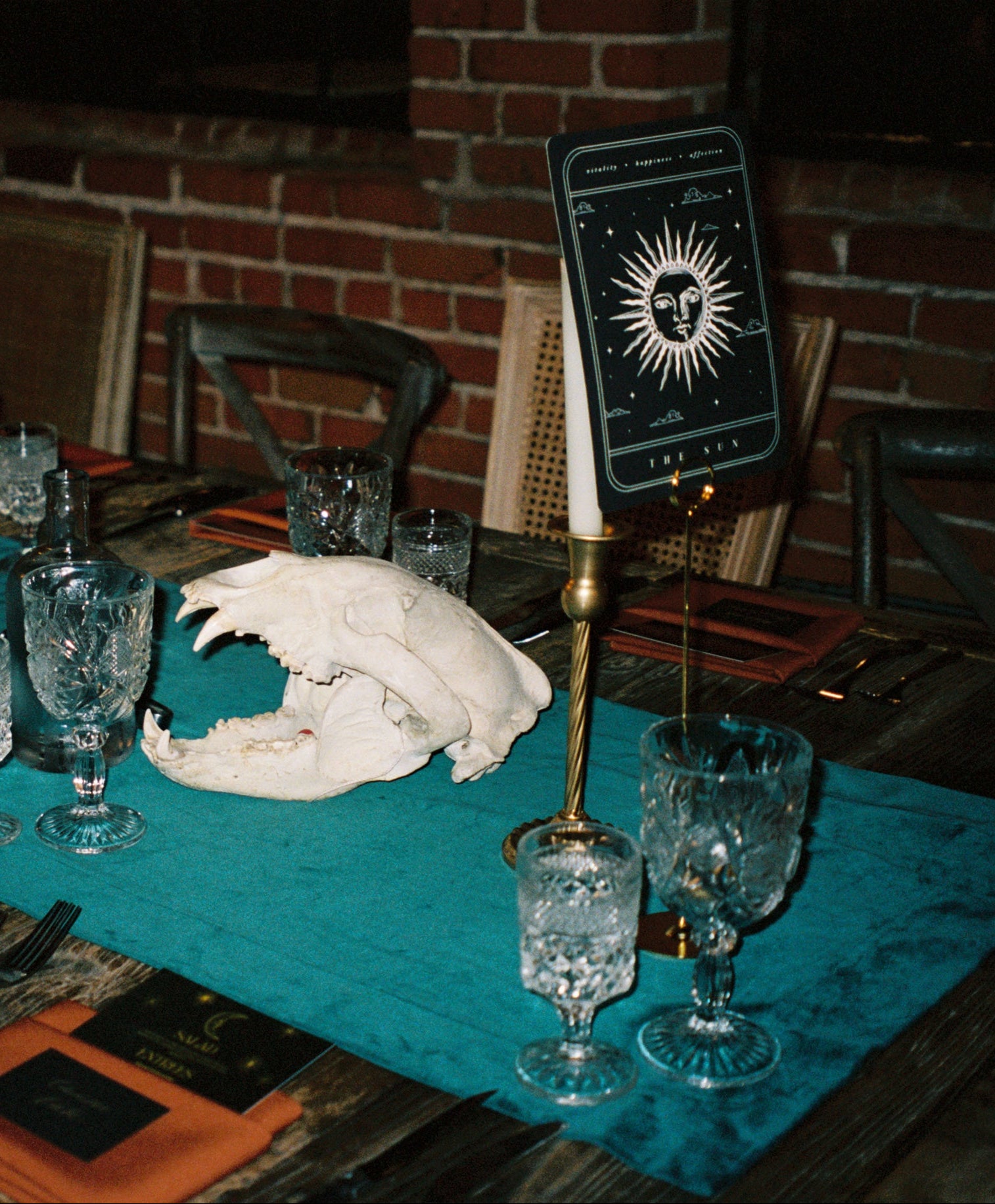 The Sun Tarot Wedding Table Name - Dining table setup with skull, glasses, and candles in a dimly lit room.