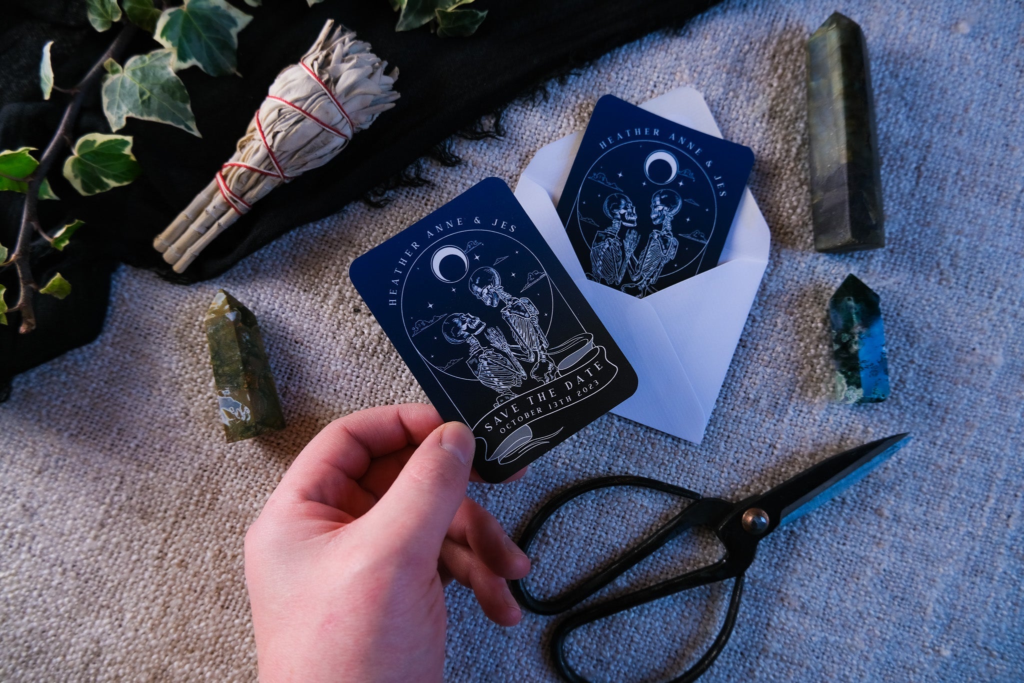 Skeleton Lovers 'Til Death Do Us Part' tarot save the date mini magnet on a table with white envelope and decorative items.