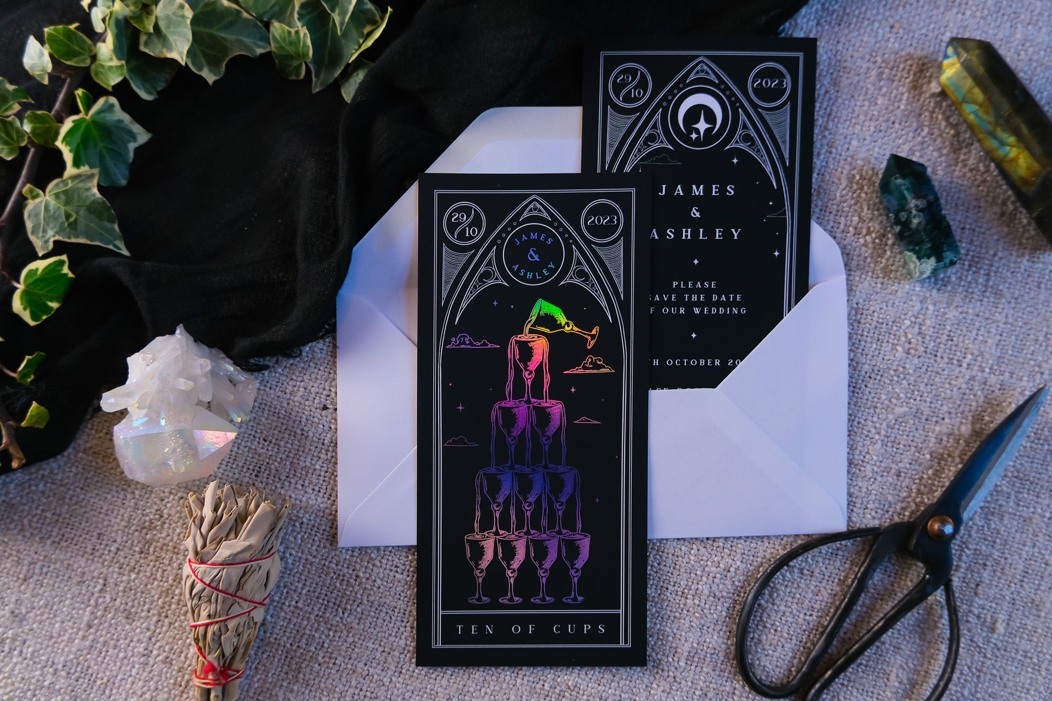 Foiled tarot card save the dates with Ten of Cups design, featuring customizable colors, paired with white envelopes.