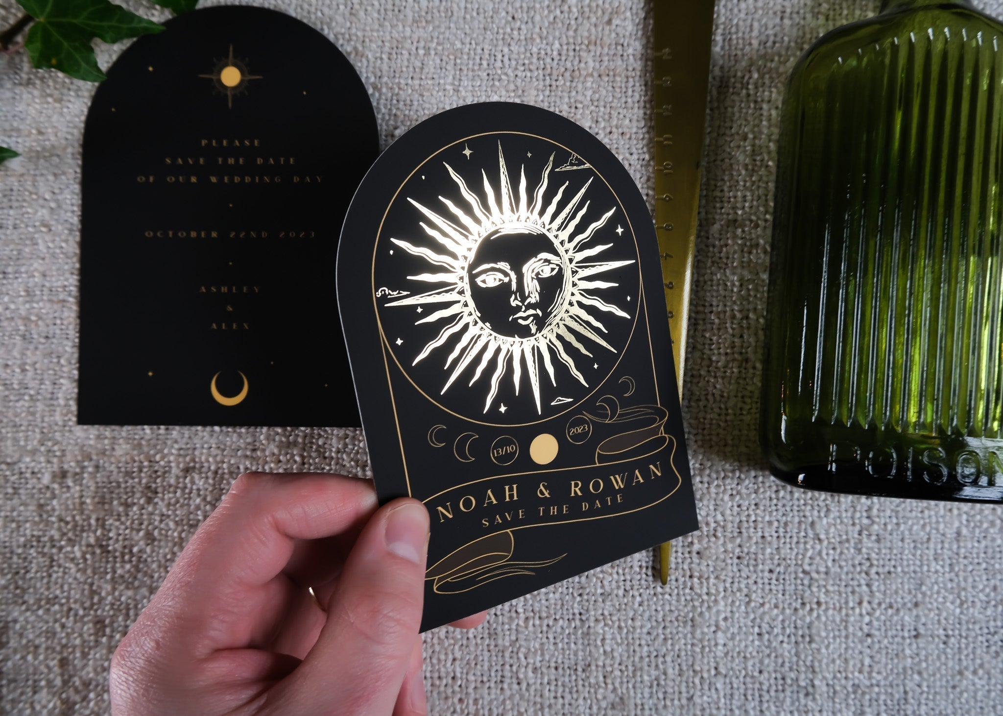 'The Sun' Tarot Arched Foiled Save The Date Card with gold foil sun design, held above textured surface.