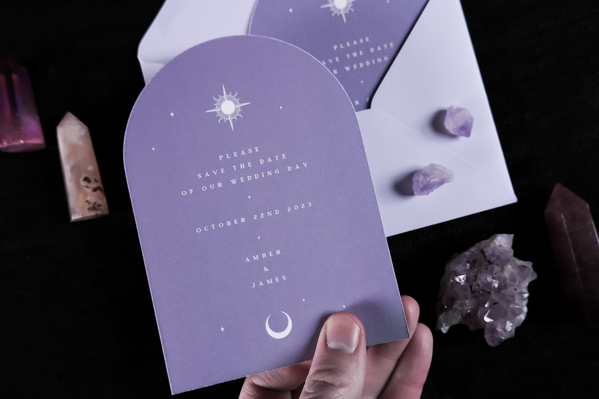 Lover Tarot Arched Save The Date Card in purple with celestial design, held by hand, accompanied by purple and brown crystals, and white envelope.