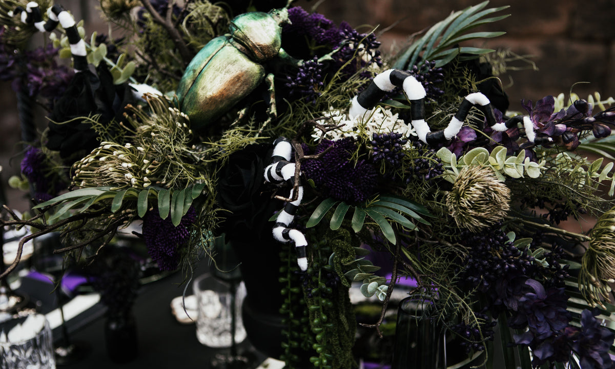 Beetlejuice inspired wedding table with dark florals, greenery, snakes, a metallic beetle and stationery