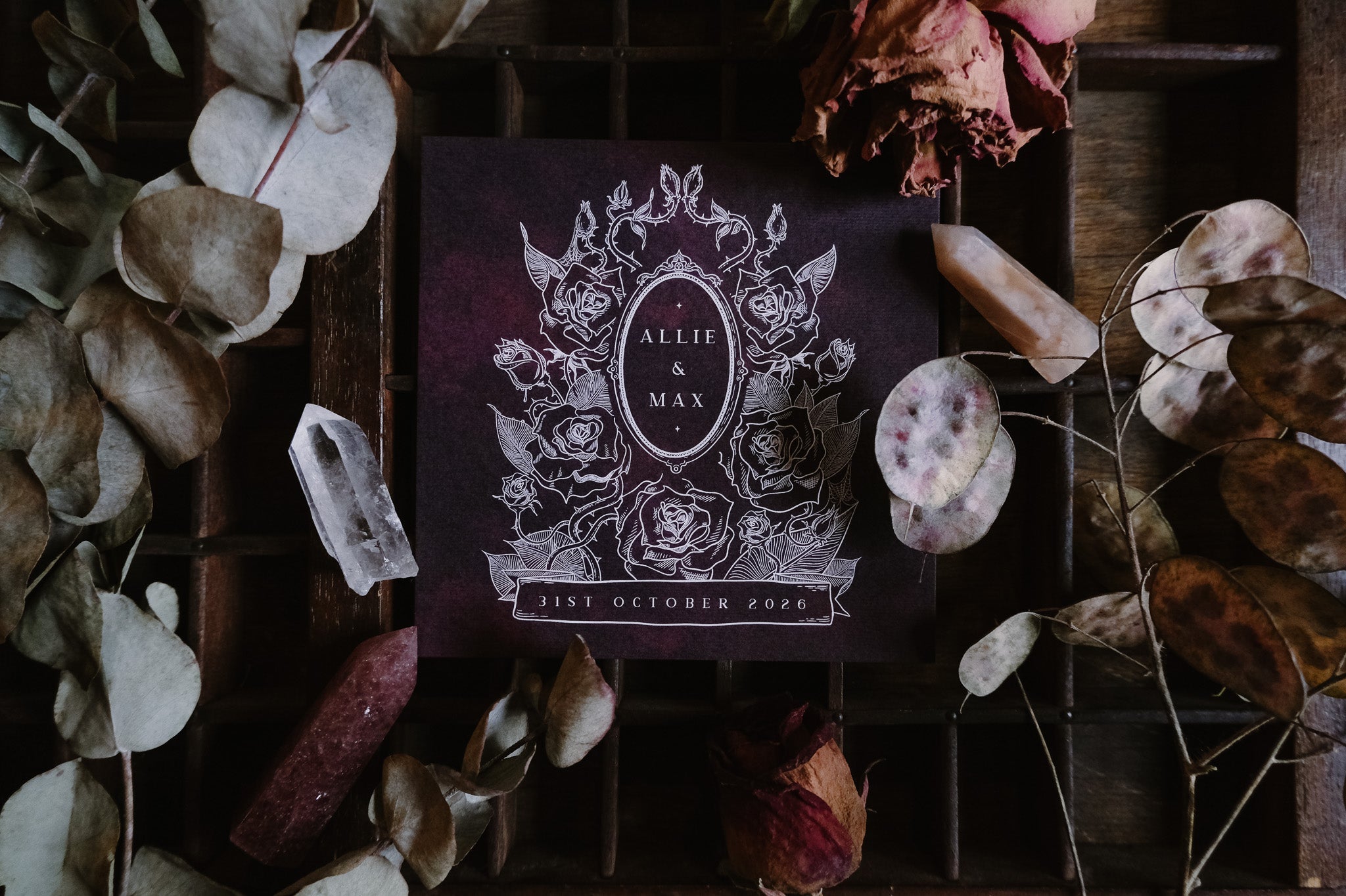 Luxury gothic save the date card with dark floral Victorian motif, accented by dried leaves and crystals for dramatic UK wedding stationery.