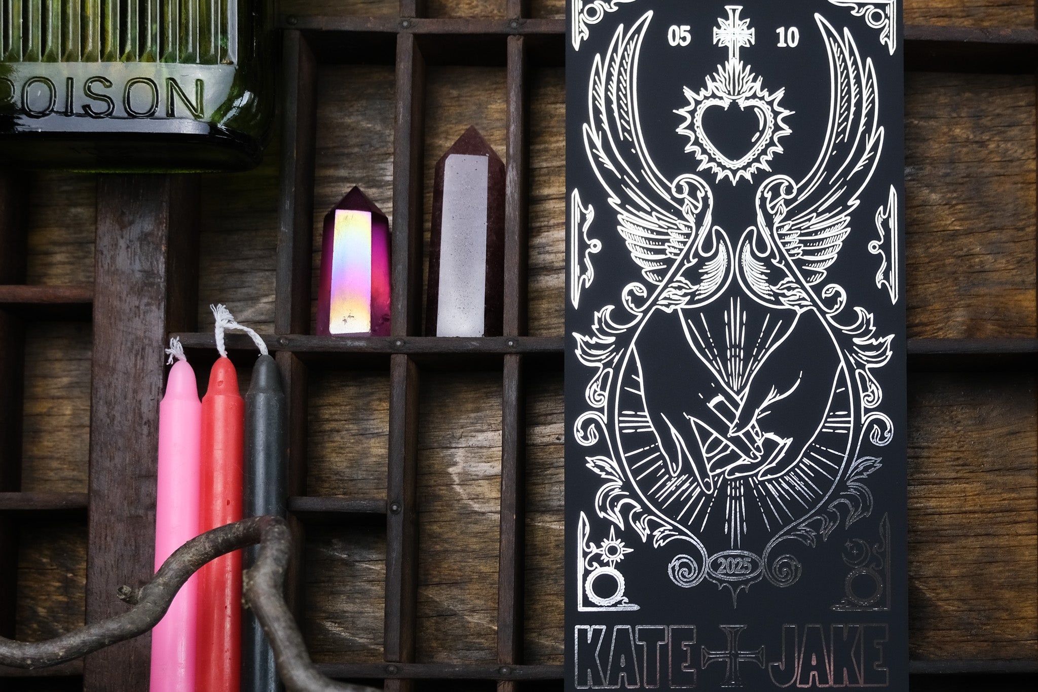 A gothic luxury foiled save the date card with dramatic celestial design, styled with pink candles and vintage crystal accents on wood.