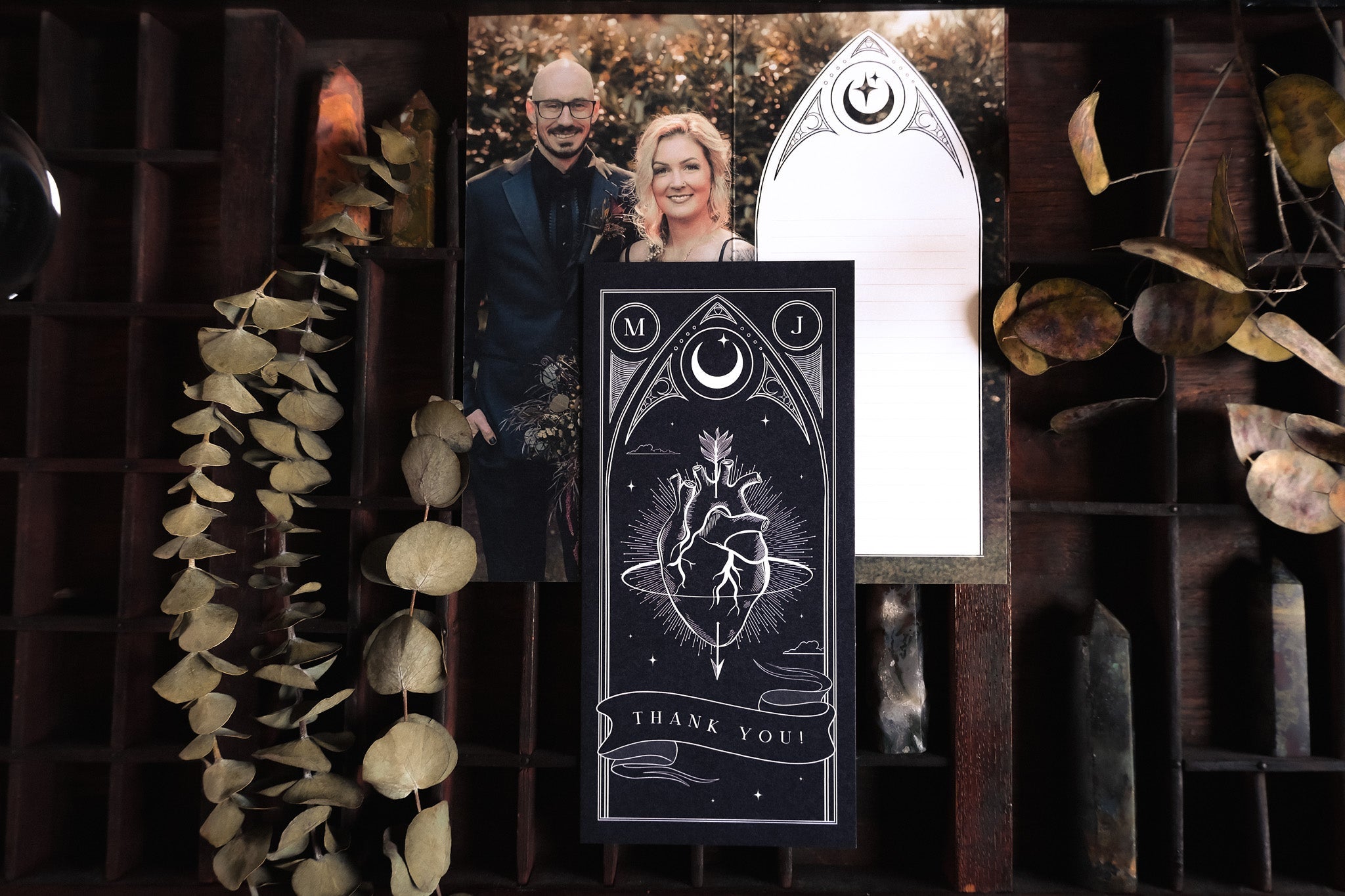 Luxury UK wedding thank you cards with mystical, gothic designs displayed amid dried leaves and crystals for a dramatic touch.