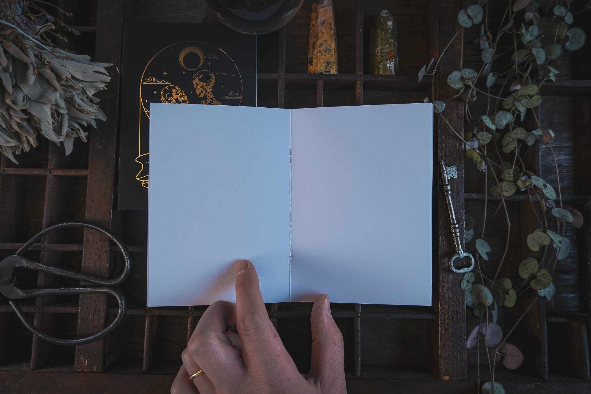 A hand opens a luxury gold and silver foiled vow book with celestial gothic design, surrounded by vintage boho wedding stationery accents.