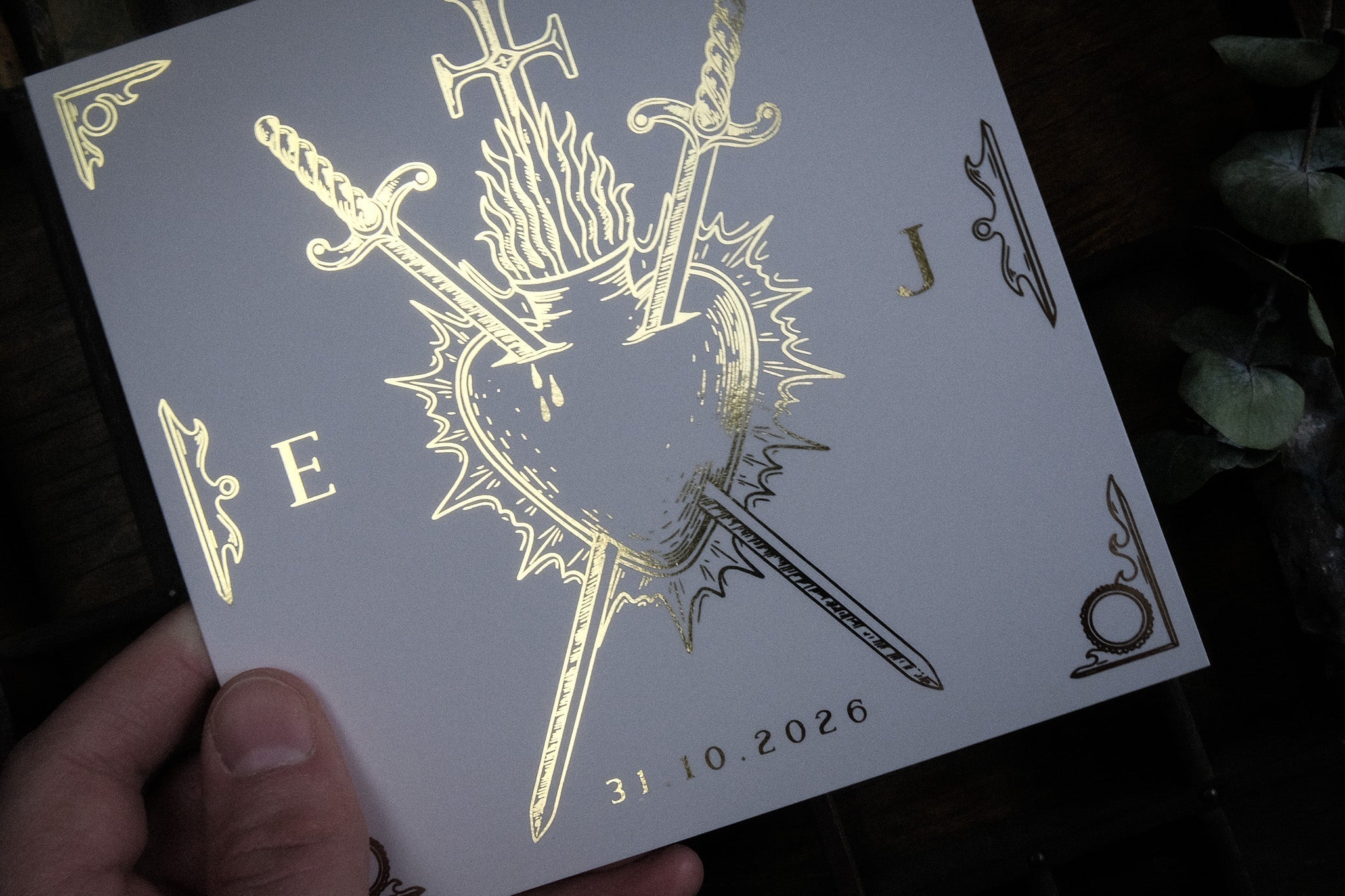 A hand displays luxury foiled wedding stationery with a gothic bleeding heart, swords, and flames—perfect for dramatic UK weddings.