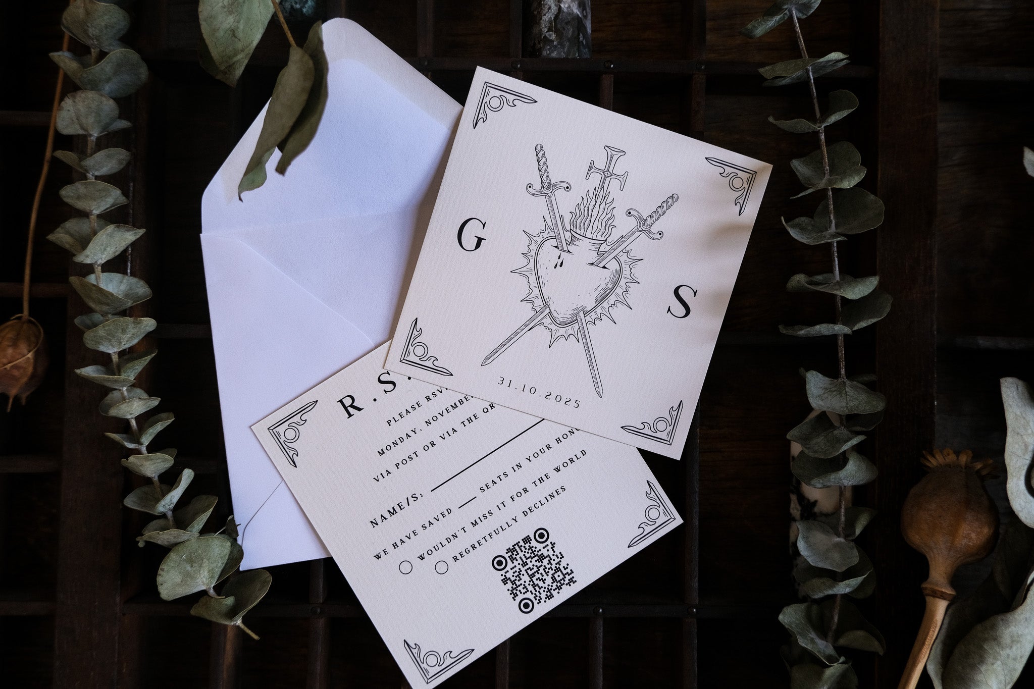 Luxury UK wedding RSVP card with romantic sword and shield design, mystical accents, displayed on wood with dried leaves and envelope.