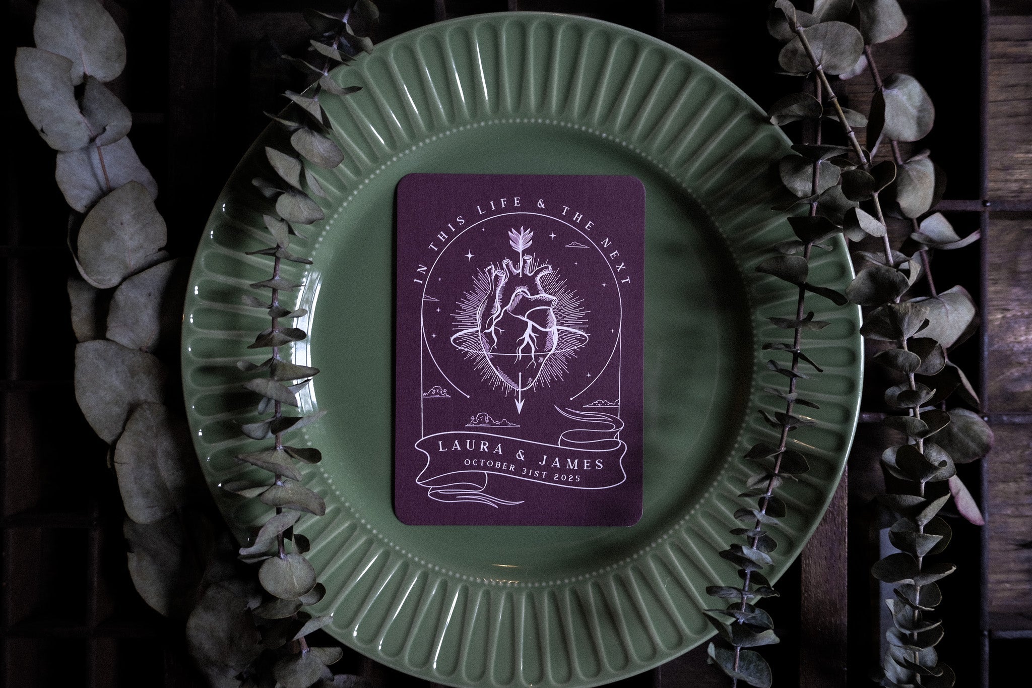 Luxury gothic wedding menu card with dramatic anatomical heart design, styled on a green plate with dried eucalyptus foliage.