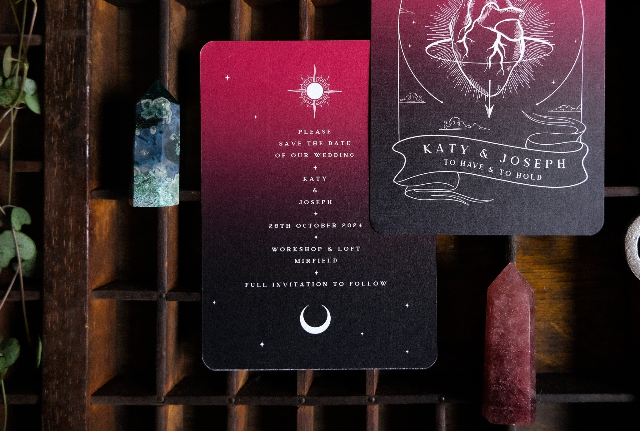 Two luxury A6 gothic save the date cards with anatomical heart motifs, set on wood amid crystals and lush green vines.