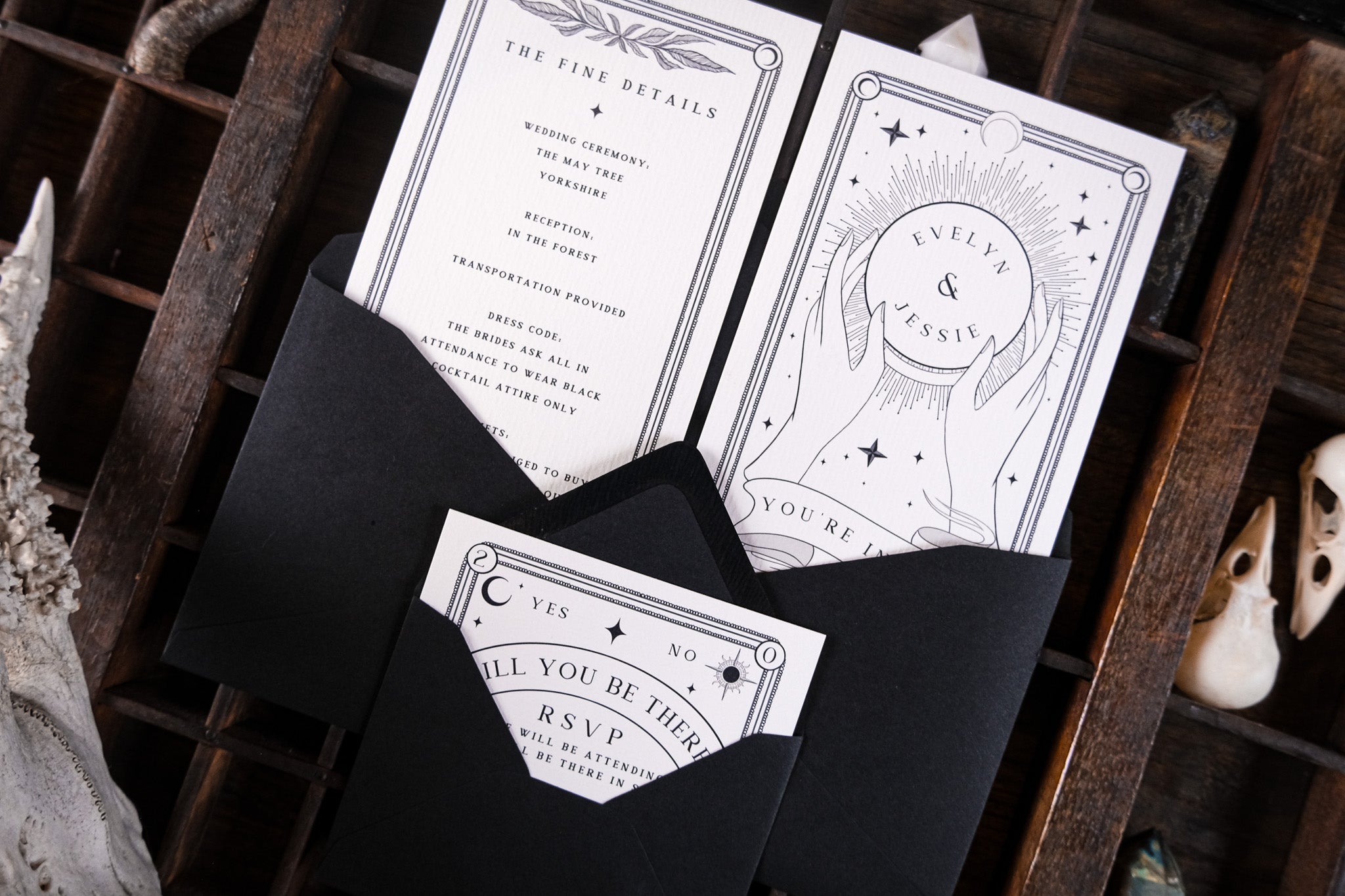 Luxury UK wedding stationery: black envelopes with gothic celestial designs, tarot-inspired, on wood with mystical decor.