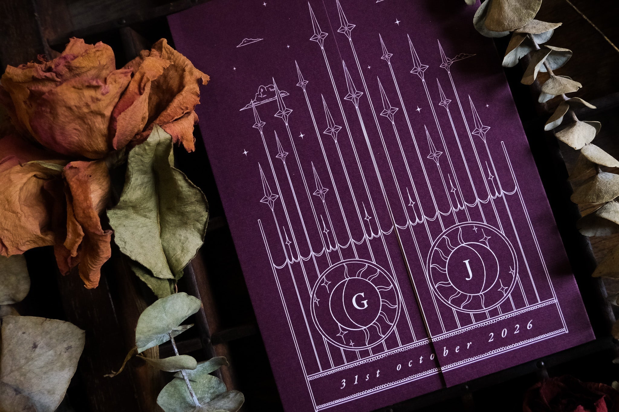 Luxury gatefold wedding invitation with a dramatic burgundy gothic design, white geometric accents, and dried floral details.