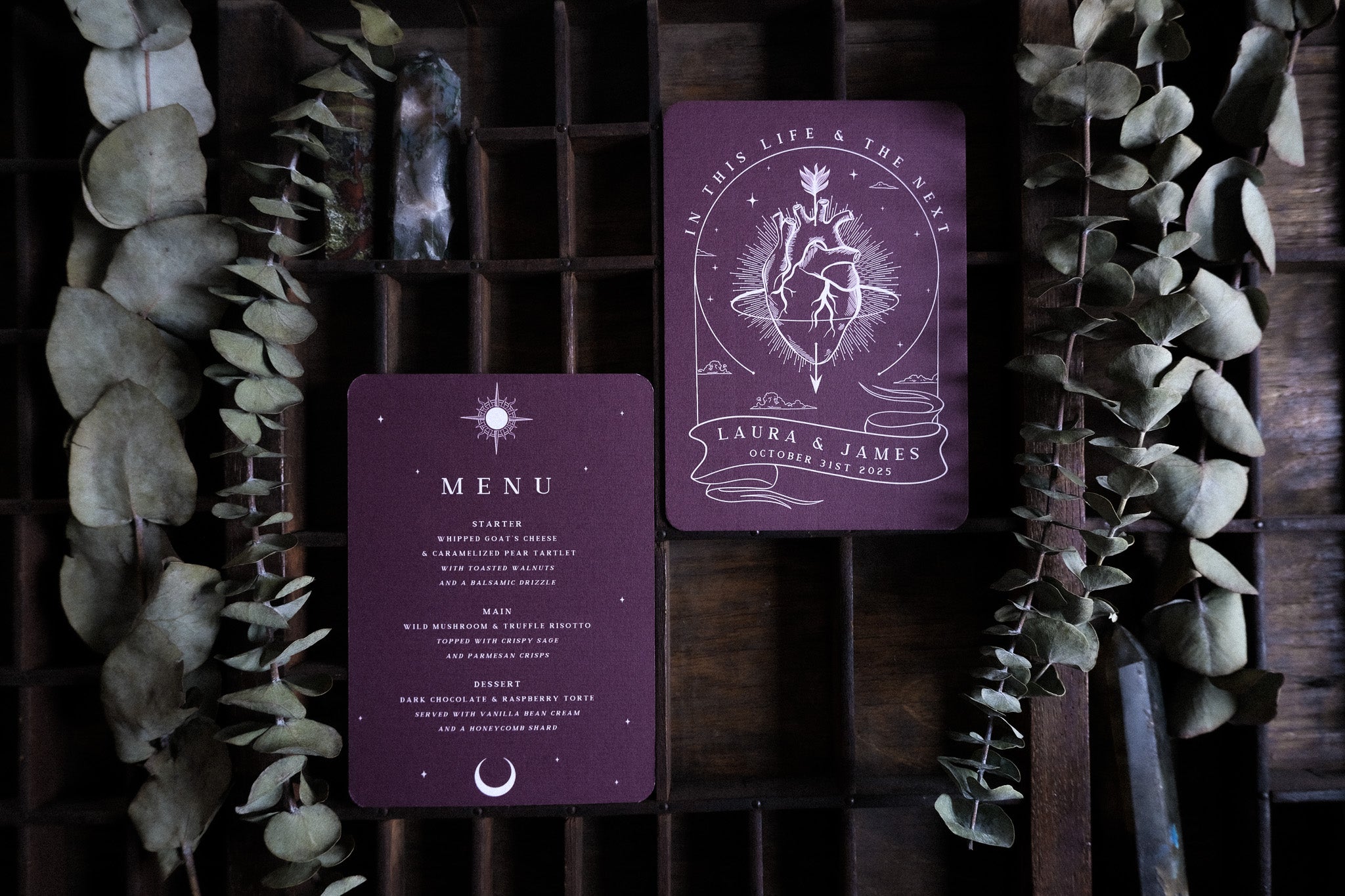 Luxury UK wedding stationery featuring gothic romantic menu and celestial invitation in deep burgundy on rustic wood with dried eucalyptus.