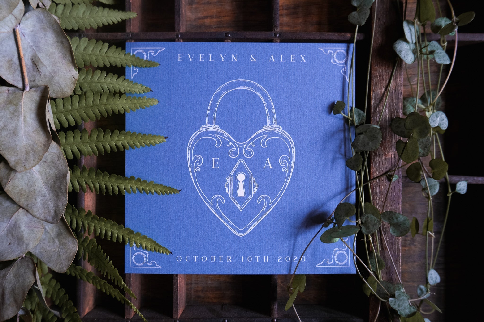 Luxury UK wedding stationery save the date card with a vintage blue Victorian design, white heart lock, and romantic leafy accents.